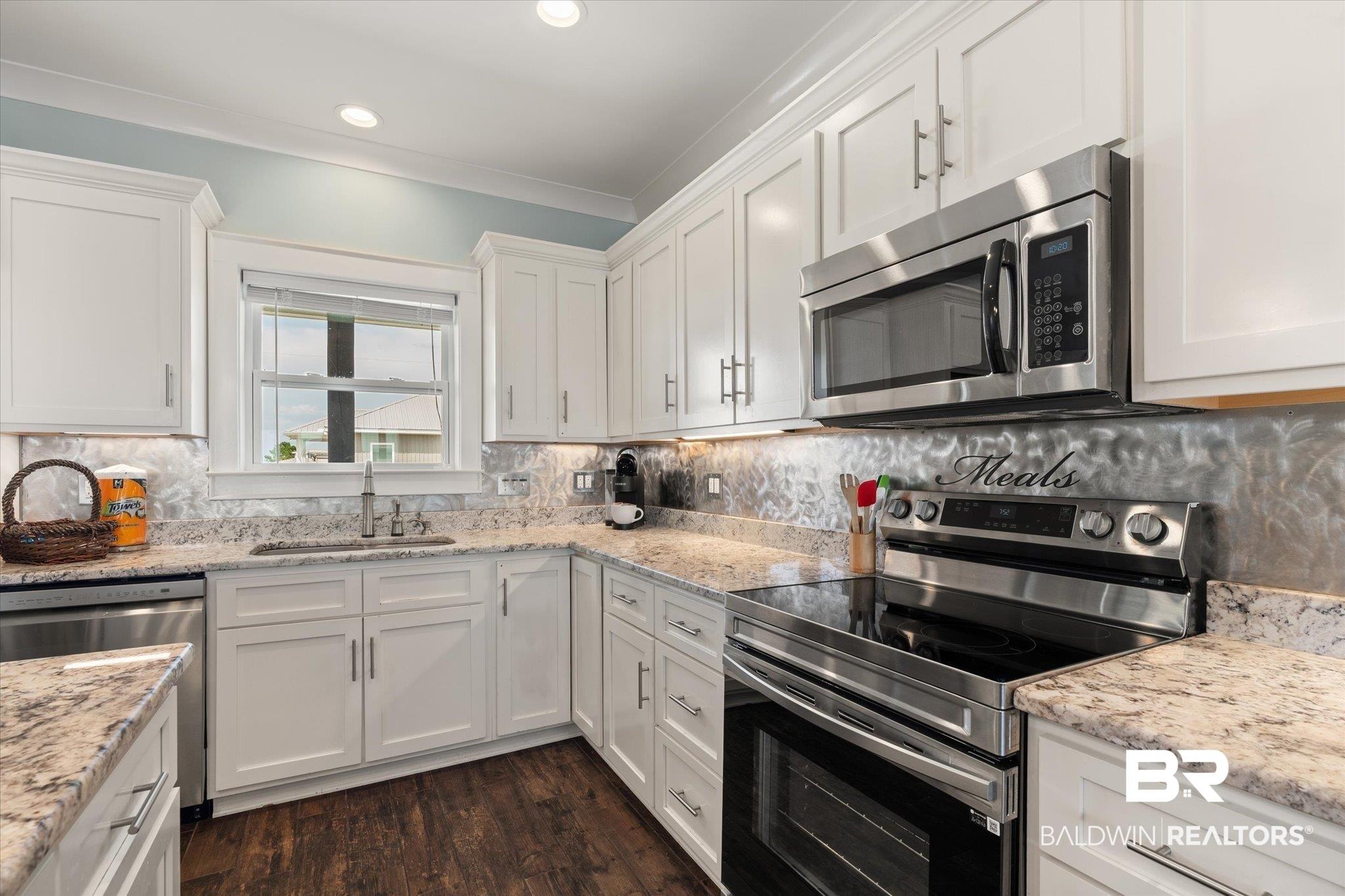 Image 4: Modern kitchen featuring white cabinetry, granite countertops, stainless steel appliances, a tile backsplash, and dark wood-finish flooring
