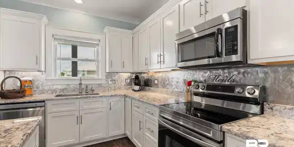 Image 4: Modern kitchen featuring white cabinetry, granite countertops, stainless steel appliances, a tile backsplash, and dark wood-finish flooring