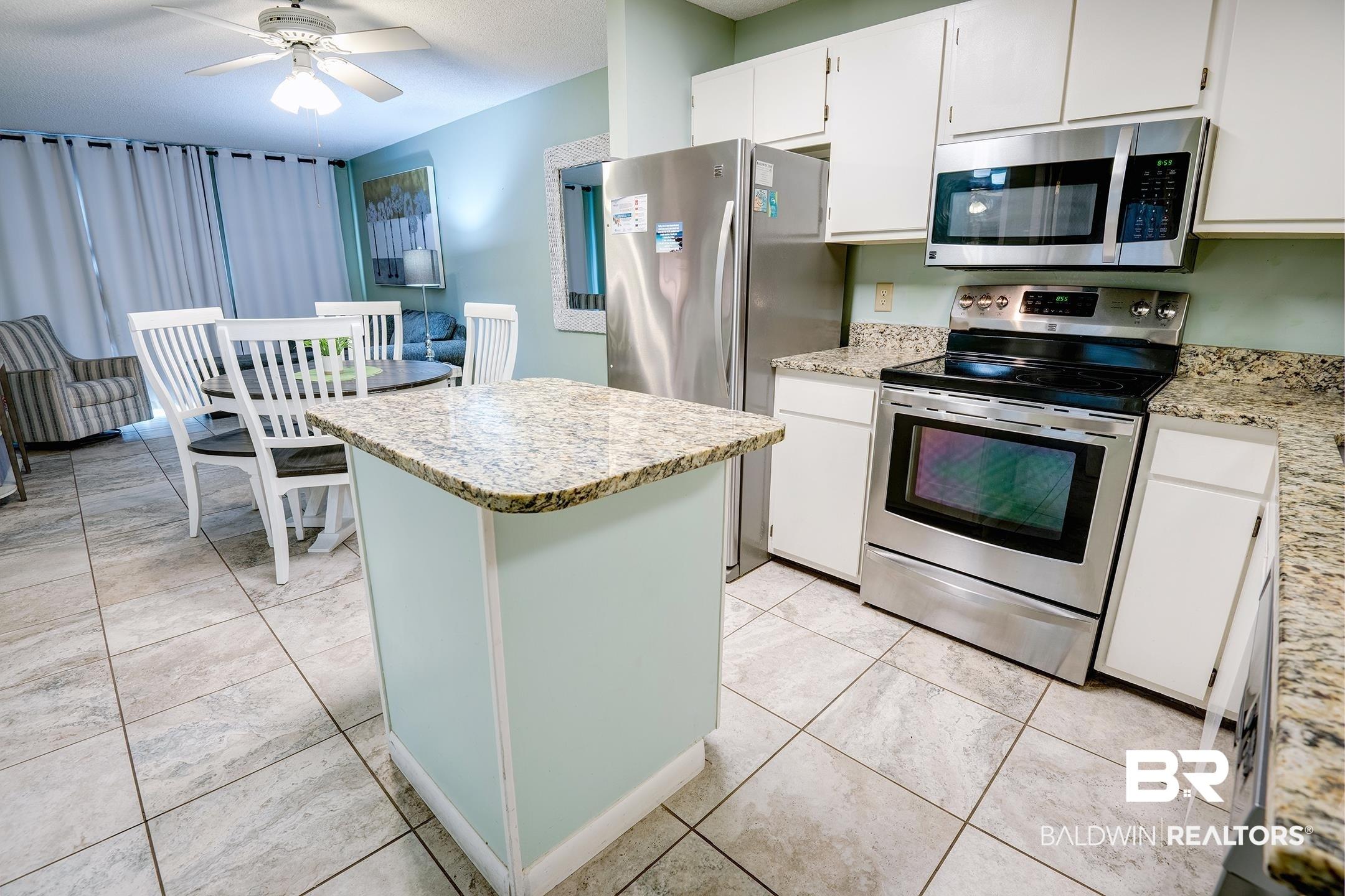 Image 2: Kitchen featuring stainless steel appliances, white cabinets, a kitchen island, light stone counters, and ceiling fan