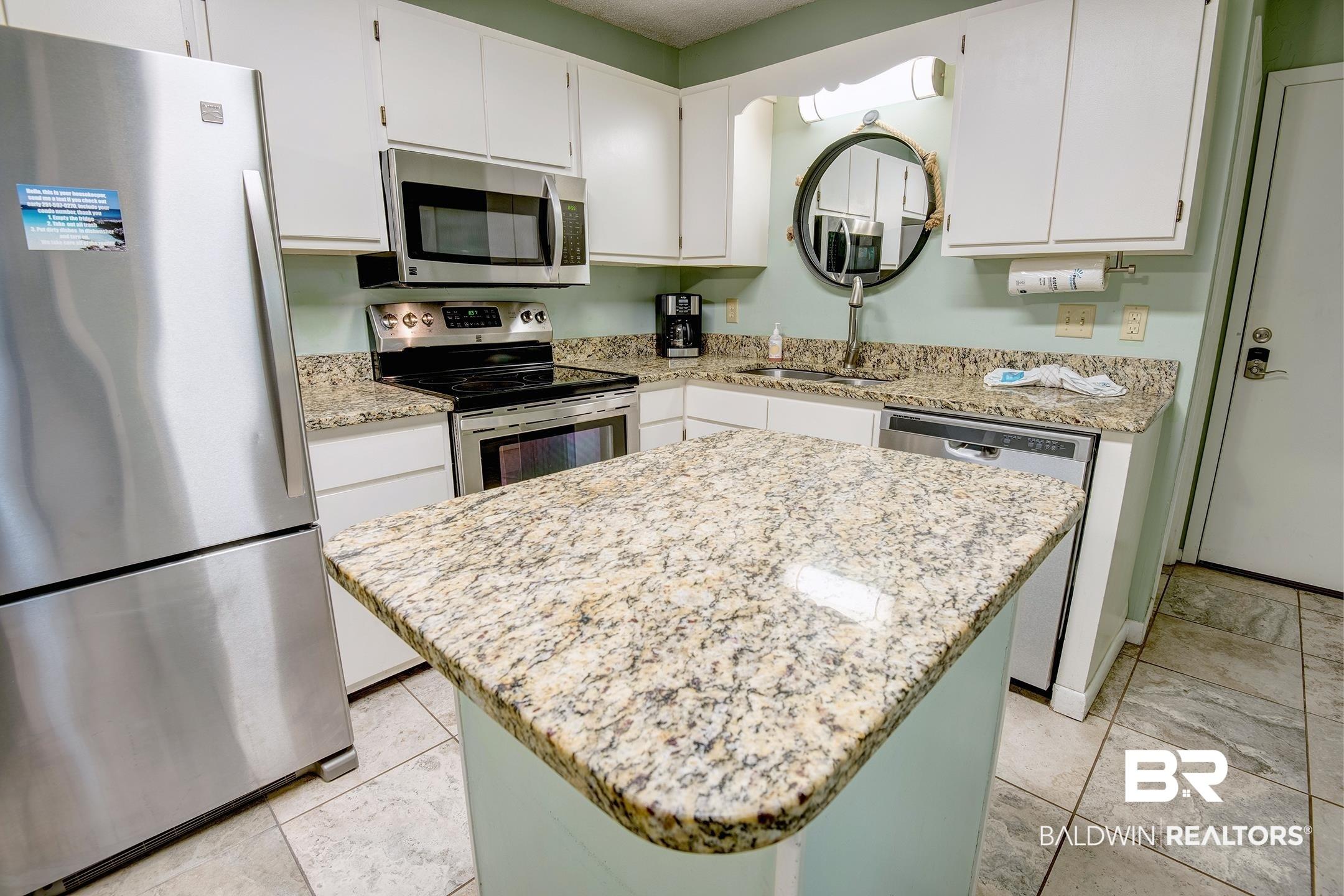Image 3: Kitchen with stainless steel appliances, light stone counters, white cabinets, and a center island