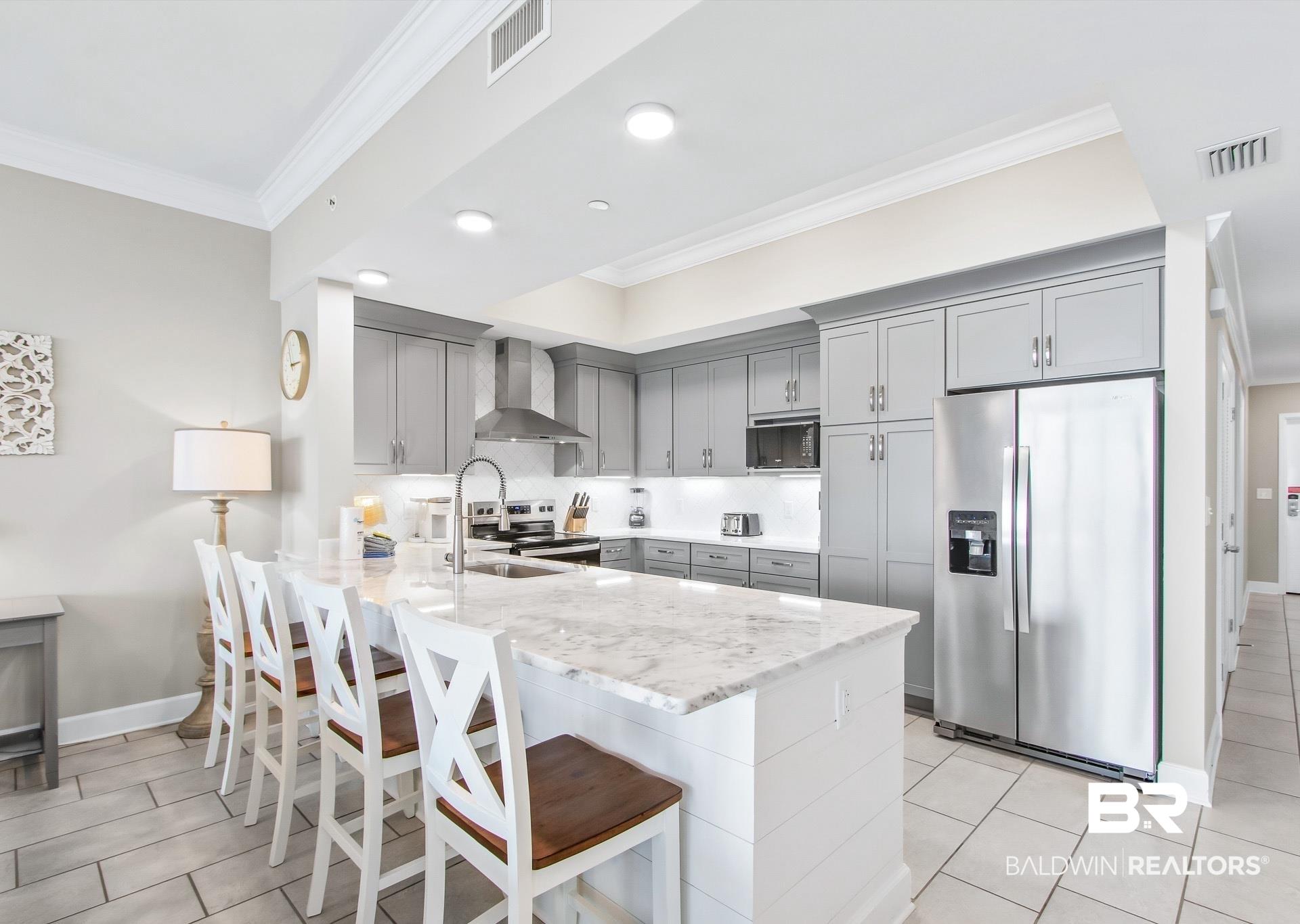 Image 4: Contemporary kitchen featuring a large island with stone countertop, stainless steel appliances, grey cabinetry, recessed lighting, and crown molding
