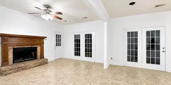 Image 4: Spacious room featuring neutral-toned tile flooring, a brick-base fireplace with a wood mantel, and multiple sets of glass-paneled French doors
