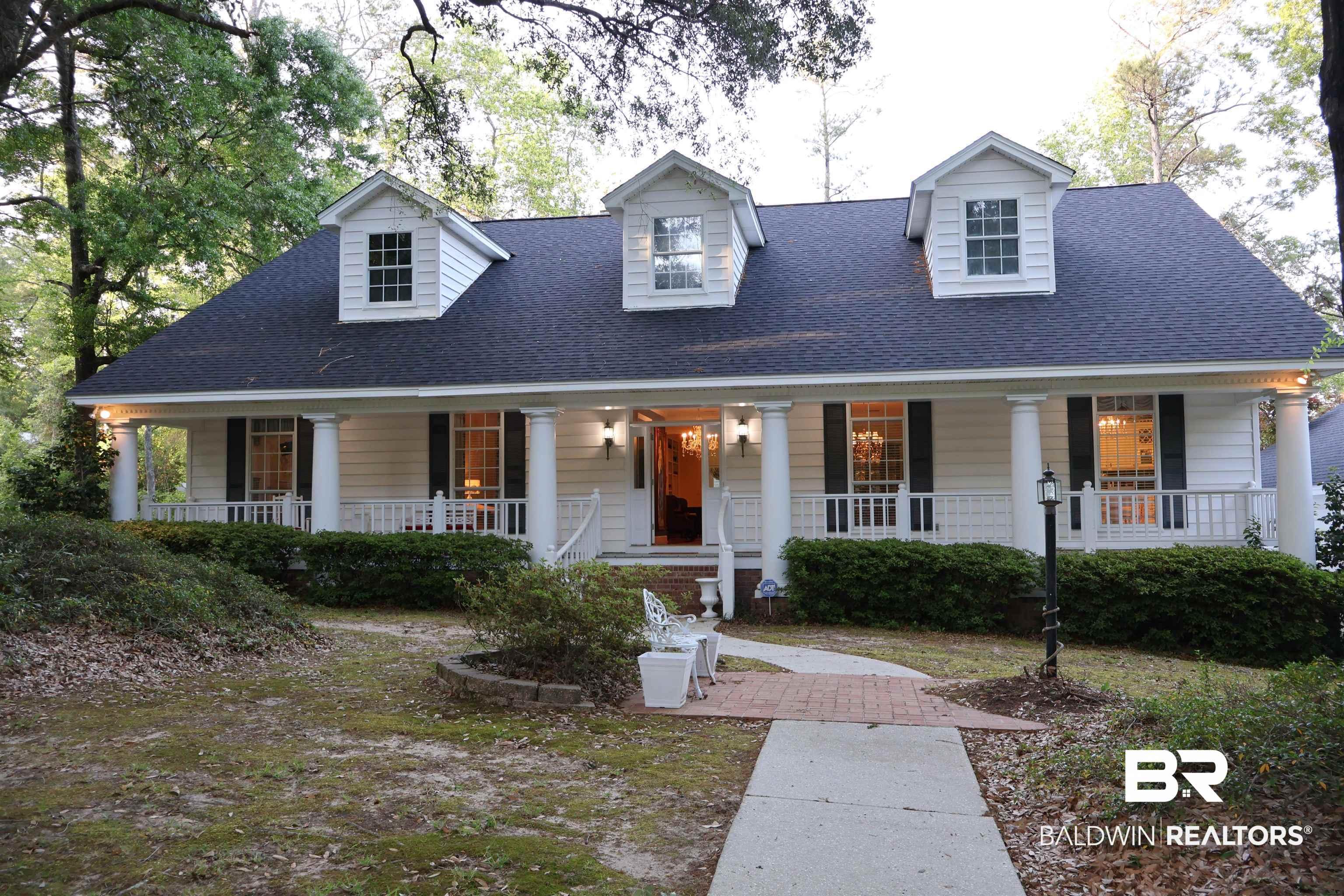 Image 2: Traditional-style residence featuring a prominent front porch with white columns and railings, a dark shingle roof, and three dormer windows