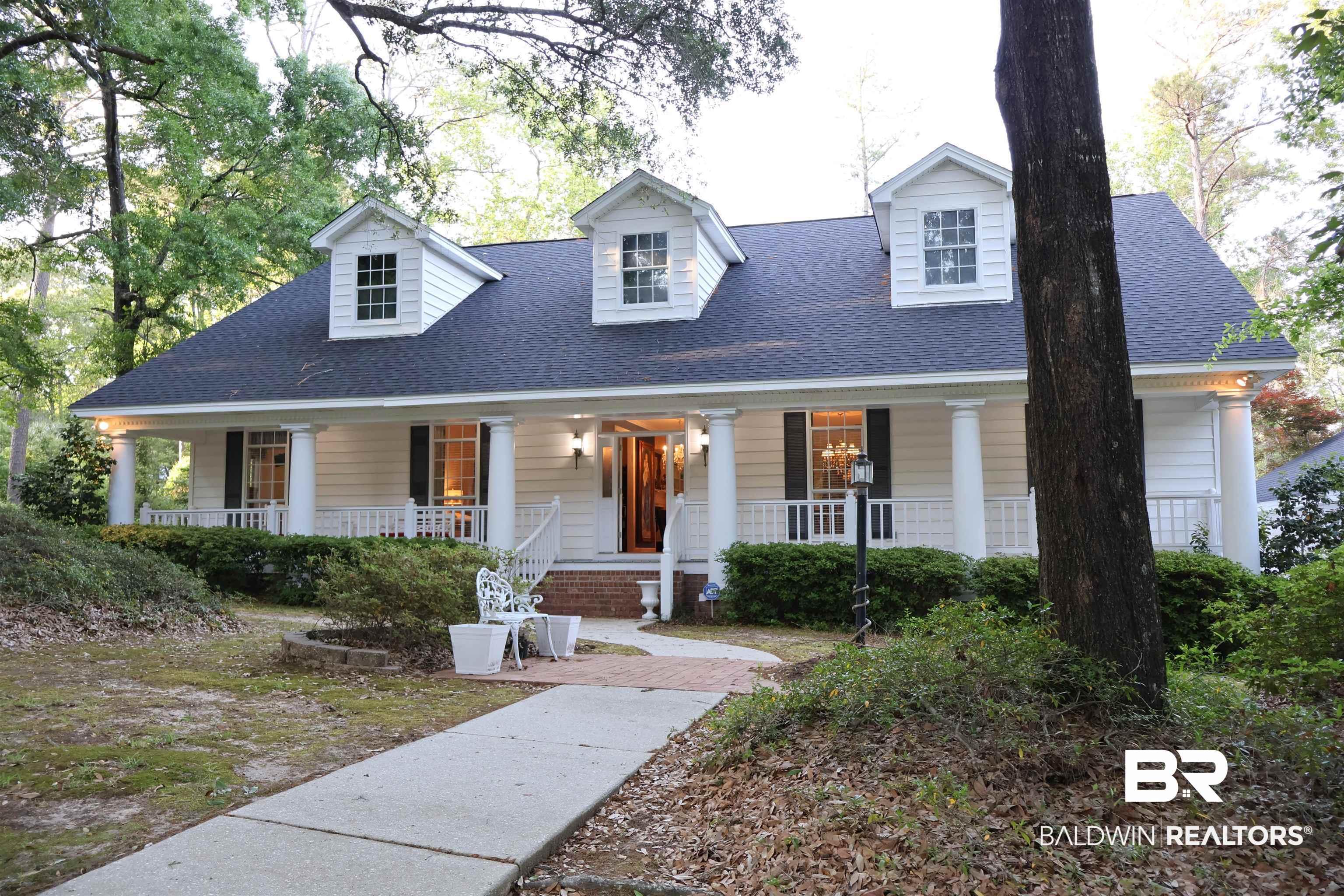 Image 3: Traditional home featuring a covered front porch with white columns and railings, dormer windows, a dark shingle roof, and a mature tree-lined setting