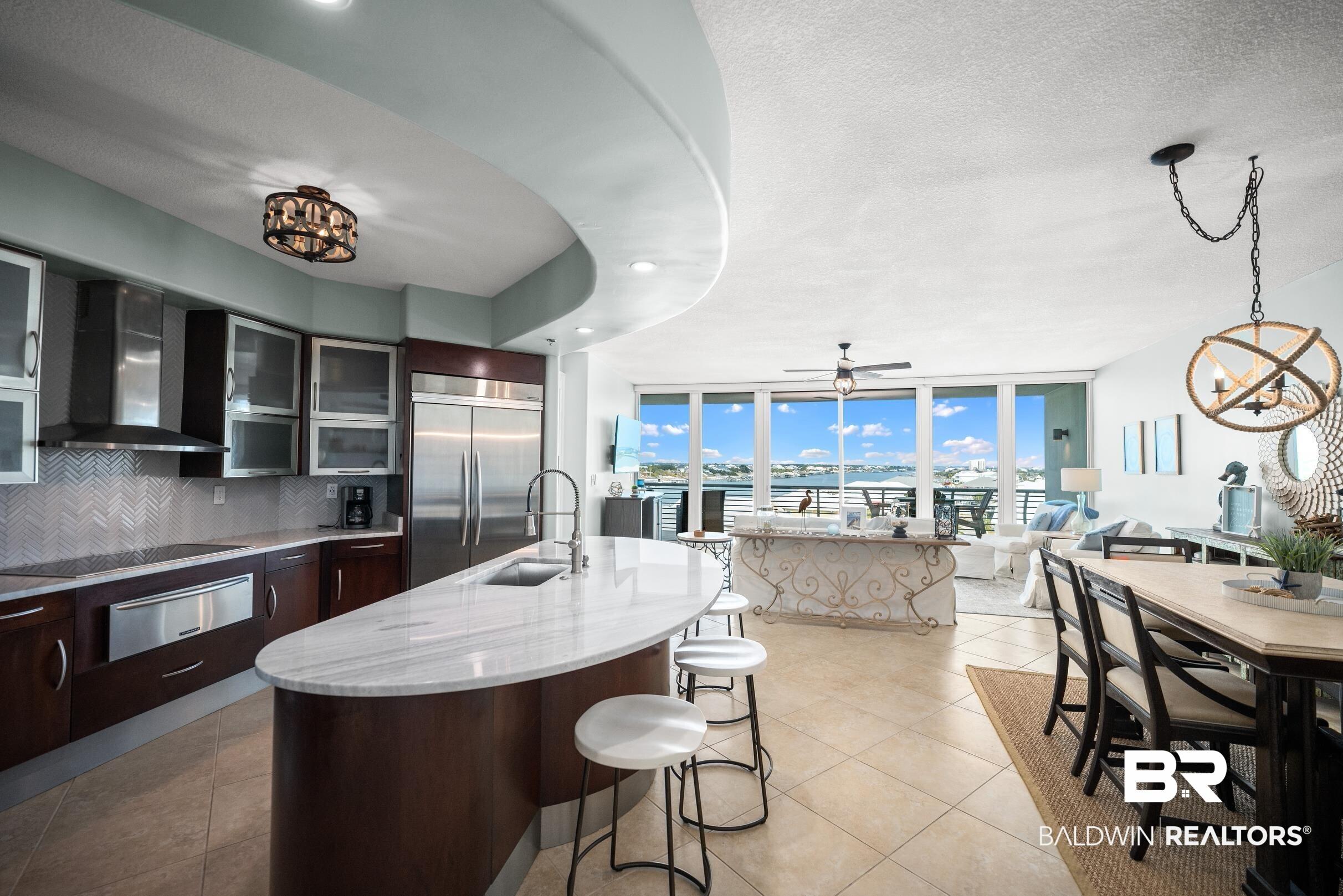 Image 2: Kitchen featuring glass insert cabinets, tasteful backsplash, a kitchen island with sink, stainless steel built in fridge, and a warming drawer
