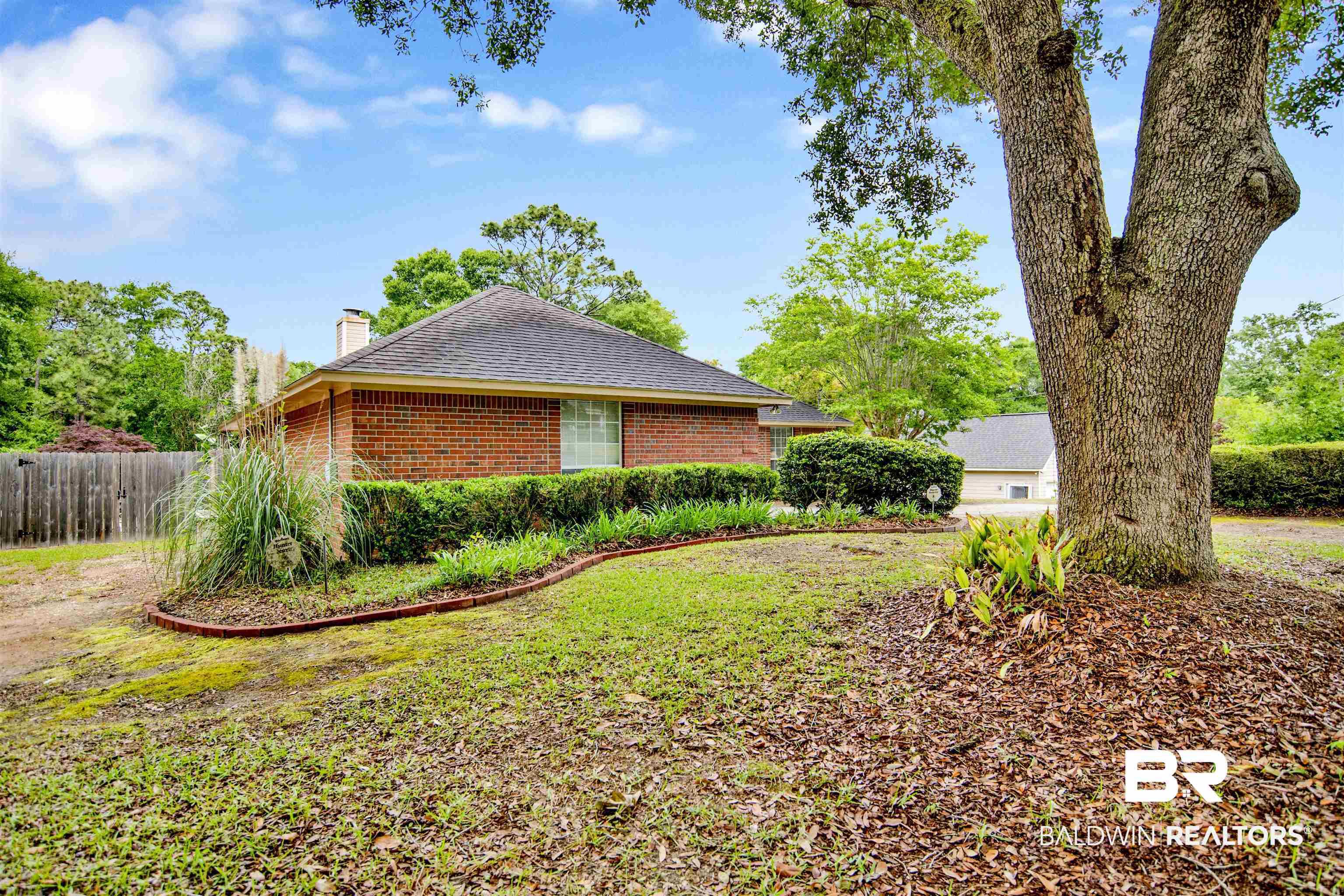 Image 3: Brick exterior with a dark shingle roof, surrounded by mature trees and established landscaping beds