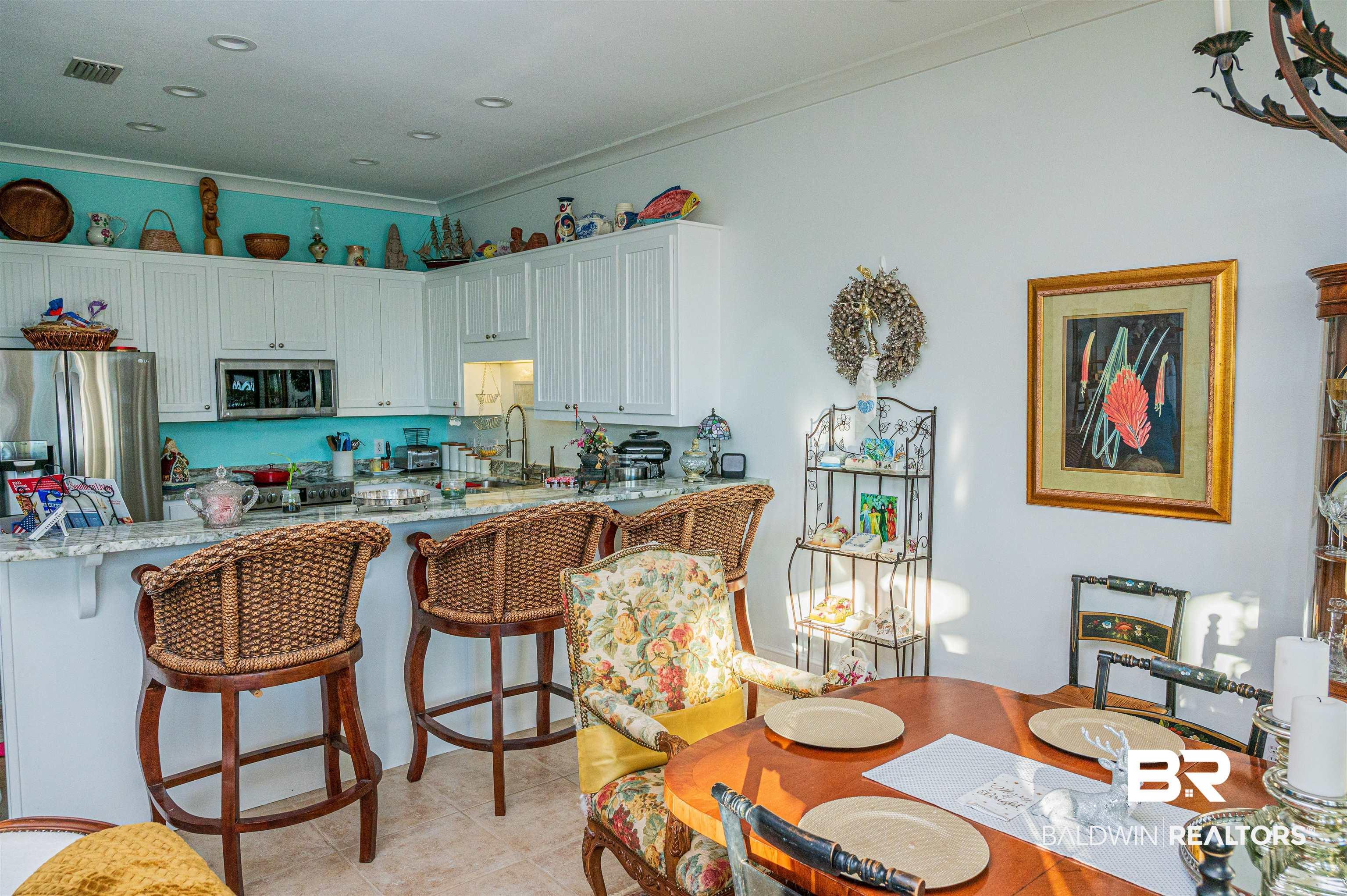 Image 3: Kitchen featuring light stone countertops, stainless steel appliances, white cabinetry, a kitchen breakfast bar, and ornamental molding