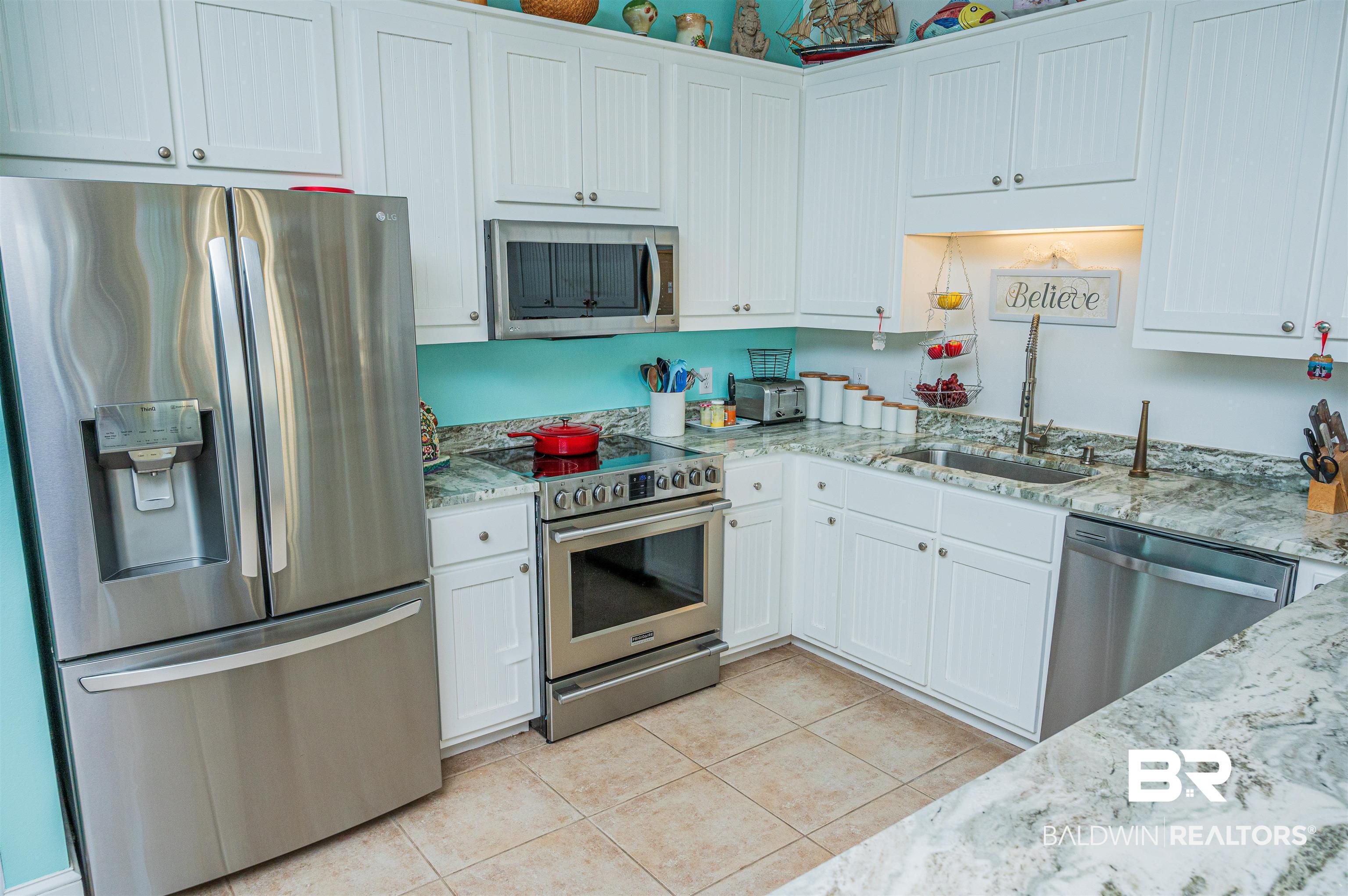 Image 4: Kitchen with stainless steel appliances, light stone counters, white cabinetry, and light tile patterned floors