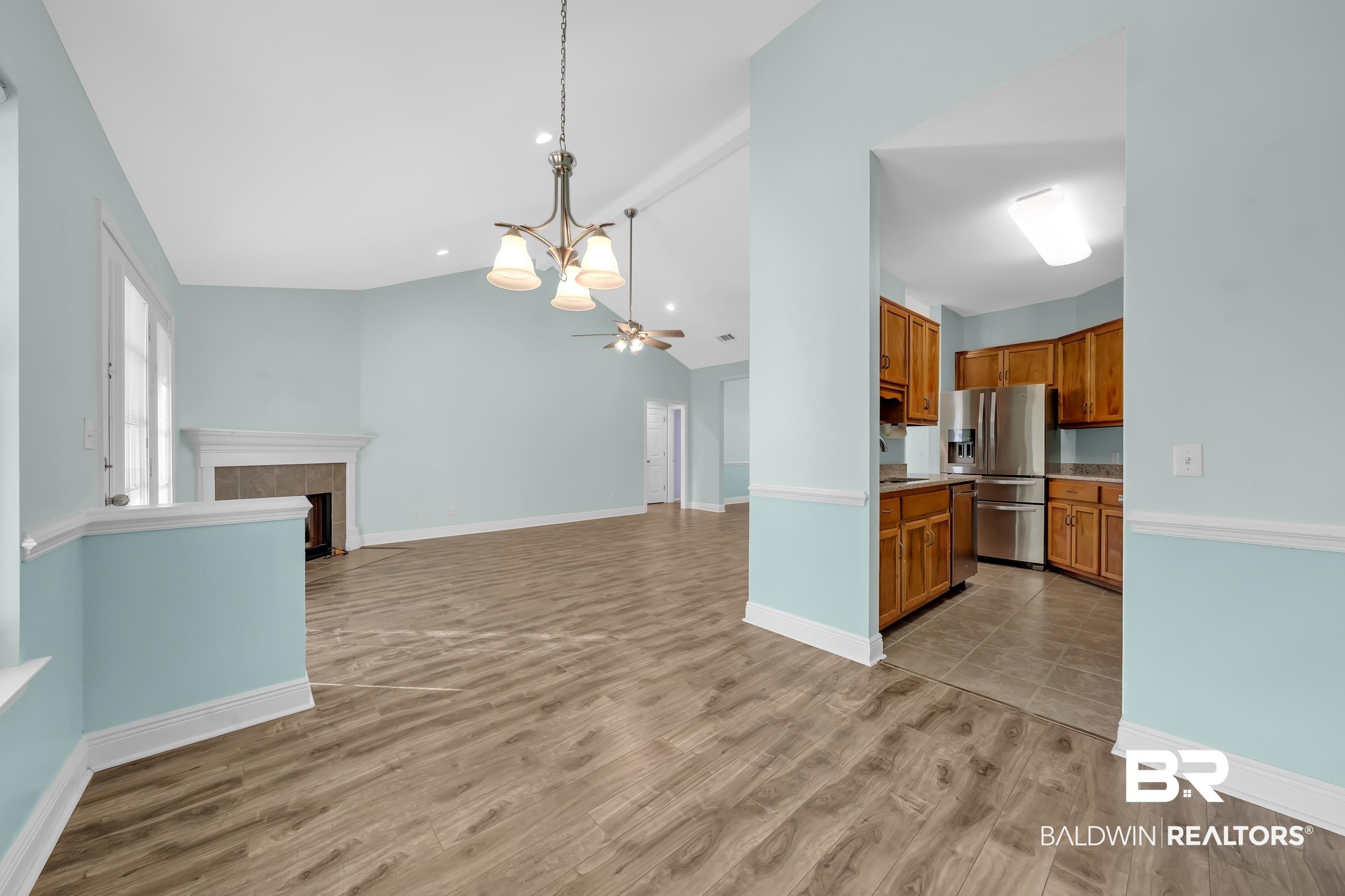 Image 4: Kitchen with brown cabinets, a chandelier, pendant lighting, vaulted ceiling, and light countertops