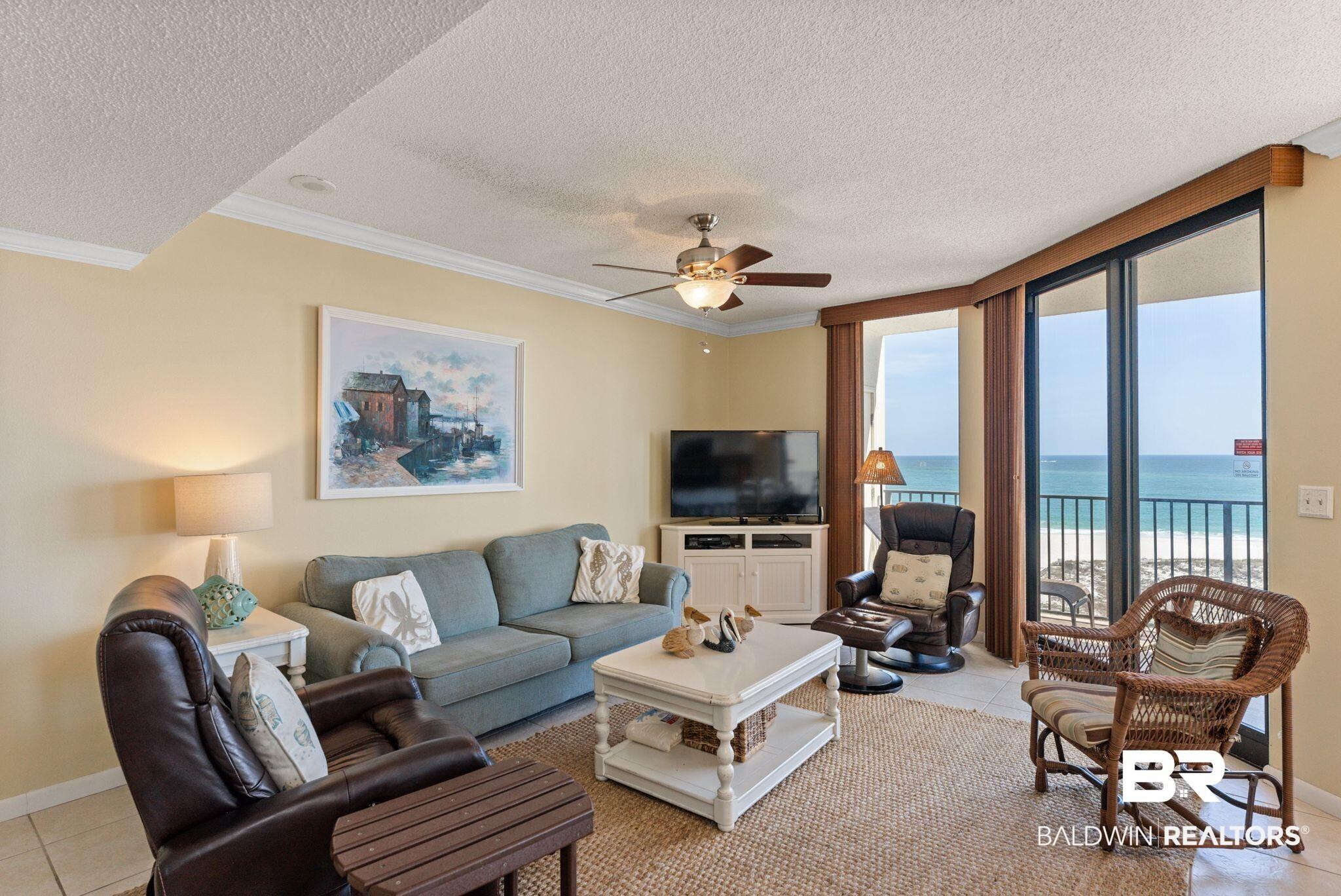 Image 3: Living area with a ceiling fan, ornamental molding, a textured ceiling, light tile patterned flooring, and expansive windows