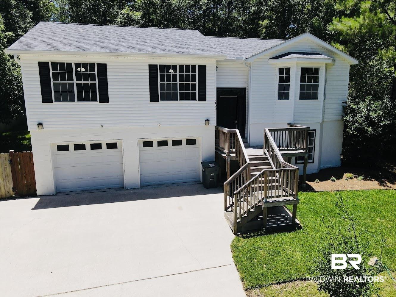 Image 2: Split-level residence featuring white siding, a two-car garage, and a wood deck entry