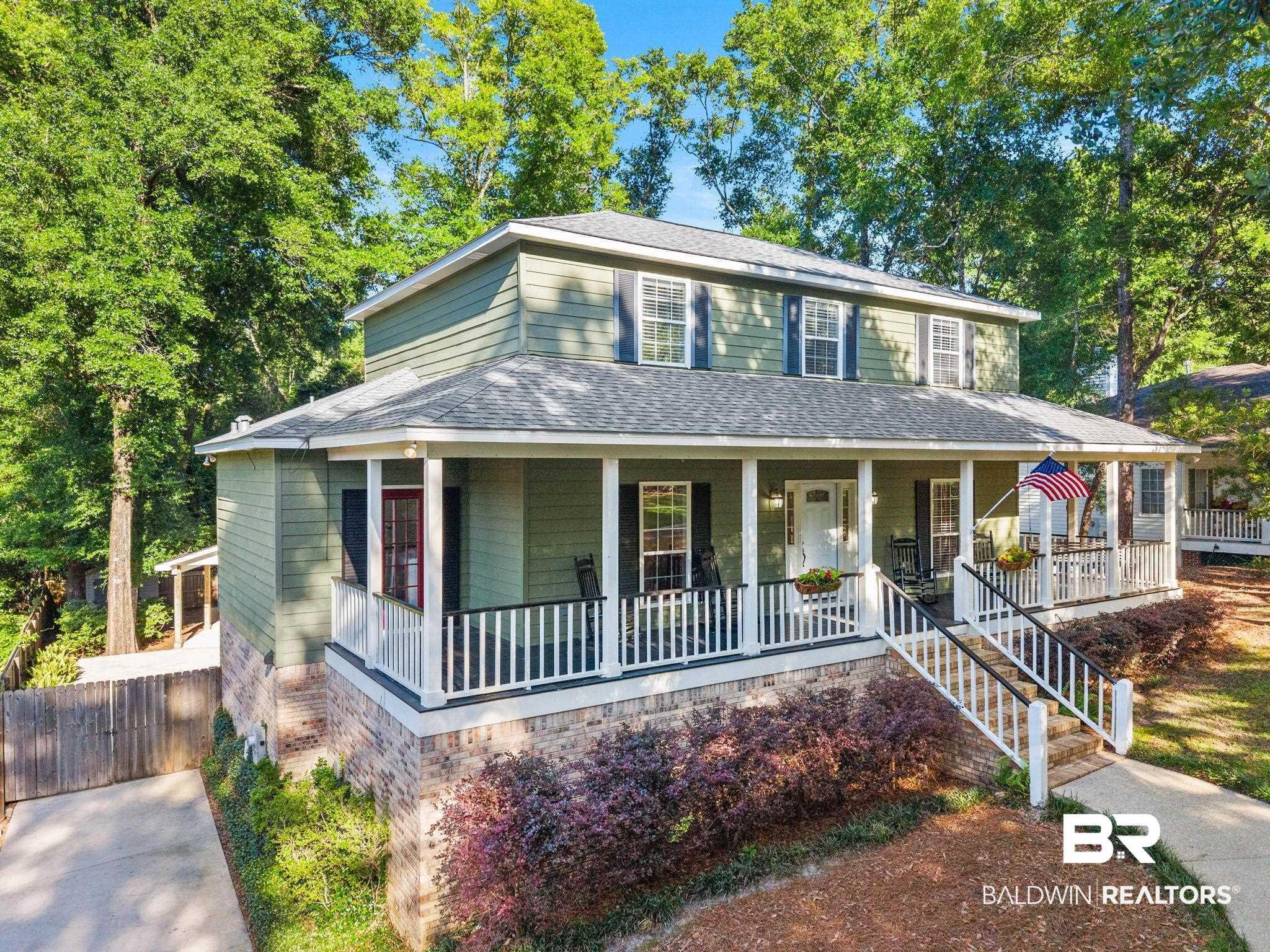 Image 2: Two-story residence featuring sage green siding and a deep front porch with white railings