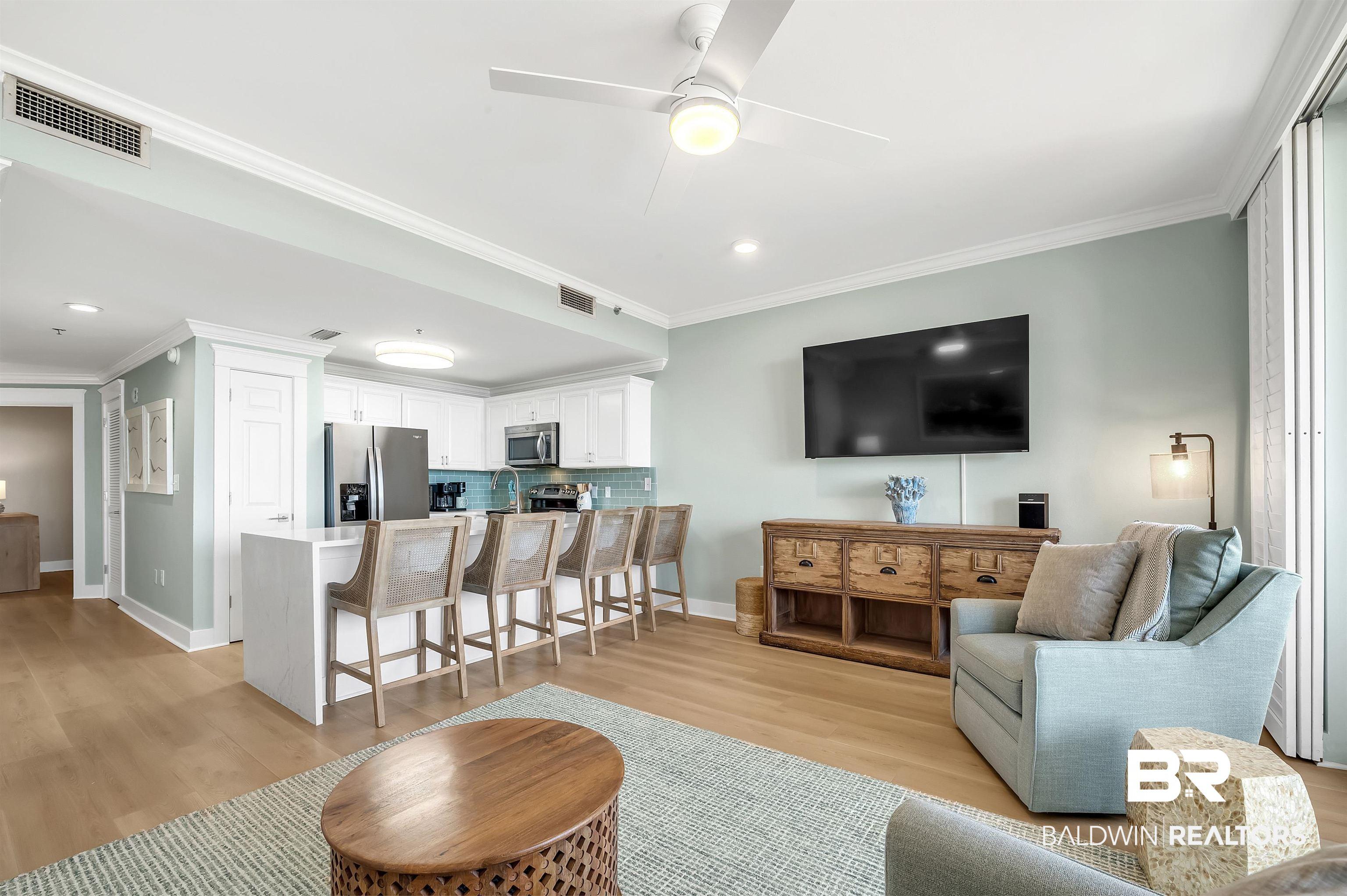 Image 2: Open-concept living space with wood-finish flooring, a contemporary ceiling fan, and crown molding
