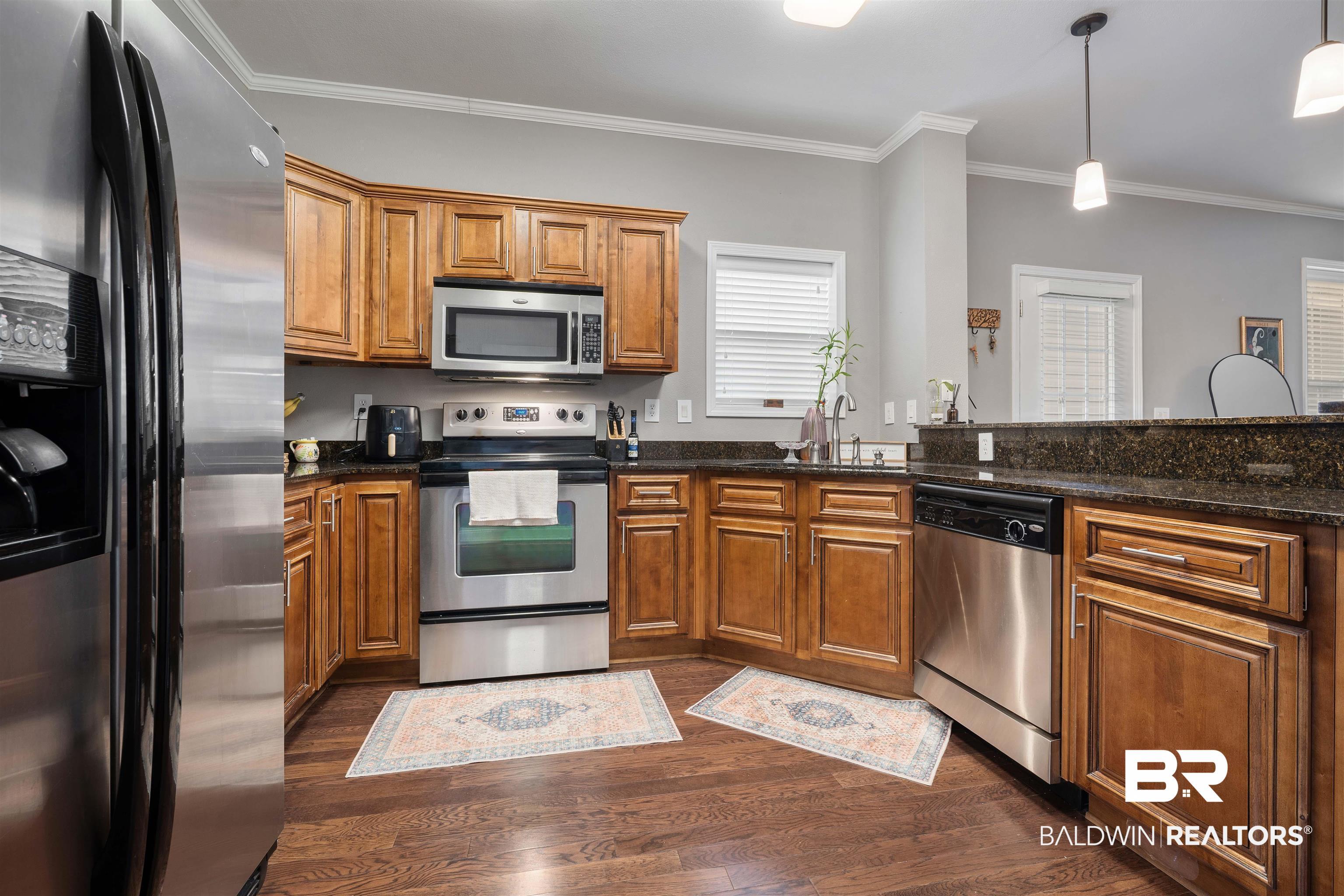 Image 3: Kitchen with stainless steel appliances, wood finish cabinetry, crown molding, dark stone countertops, and decorative light fixtures