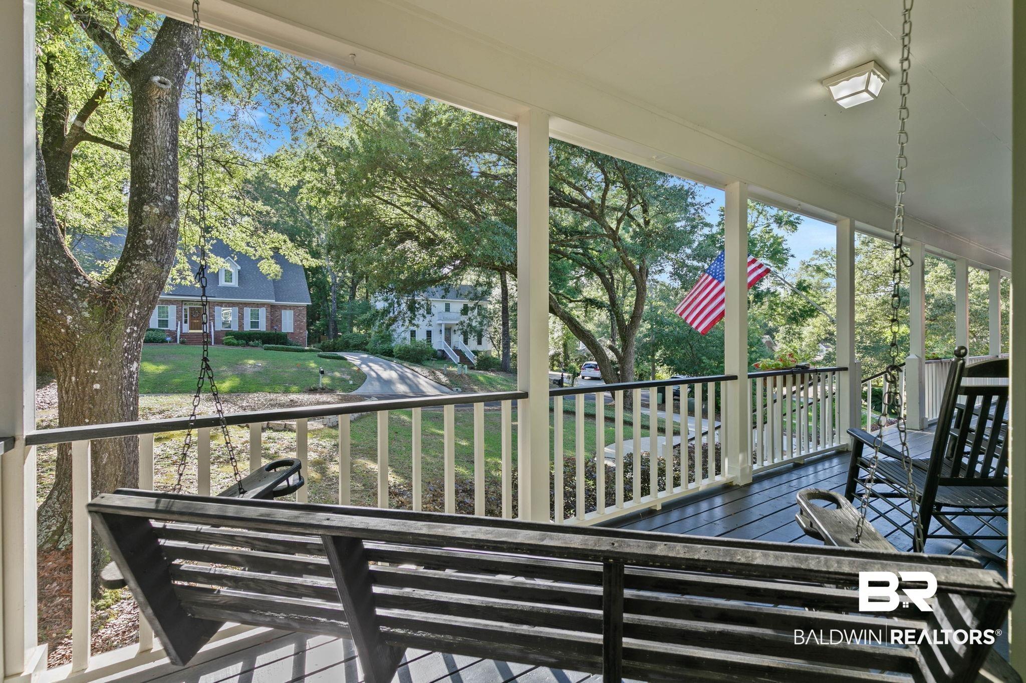 Image 4: Spacious covered porch with dark wood-finish flooring, white balusters, and a built-in porch swing