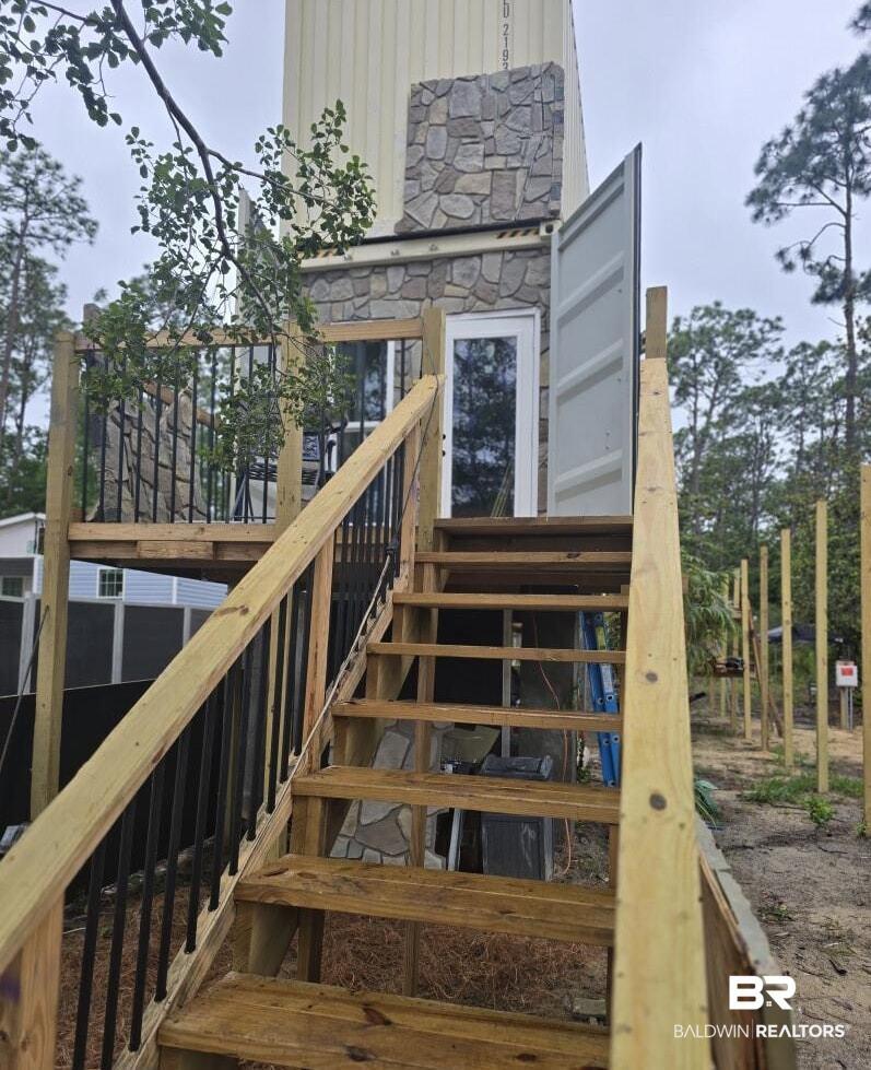 Image 2: Exterior featuring a stone-clad facade, a white paneled door with glass, a wooden deck with black metal balusters, and an exterior staircase with wooden treads and railings