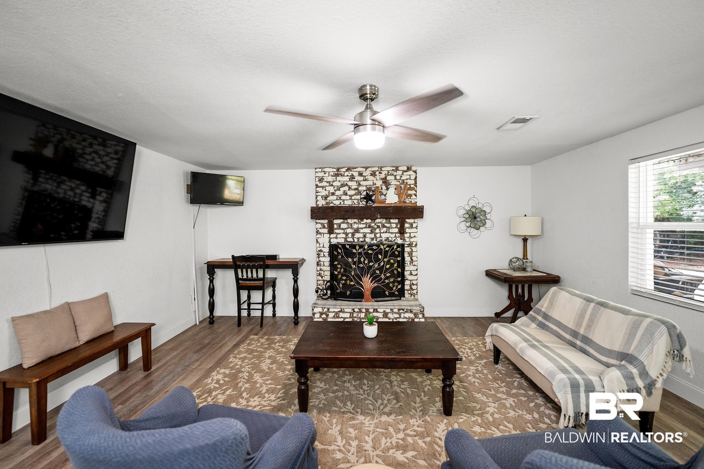 Image 3: Living area featuring wood-finish flooring, a white brick fireplace with a wood mantel, and a ceiling fan with integrated lighting