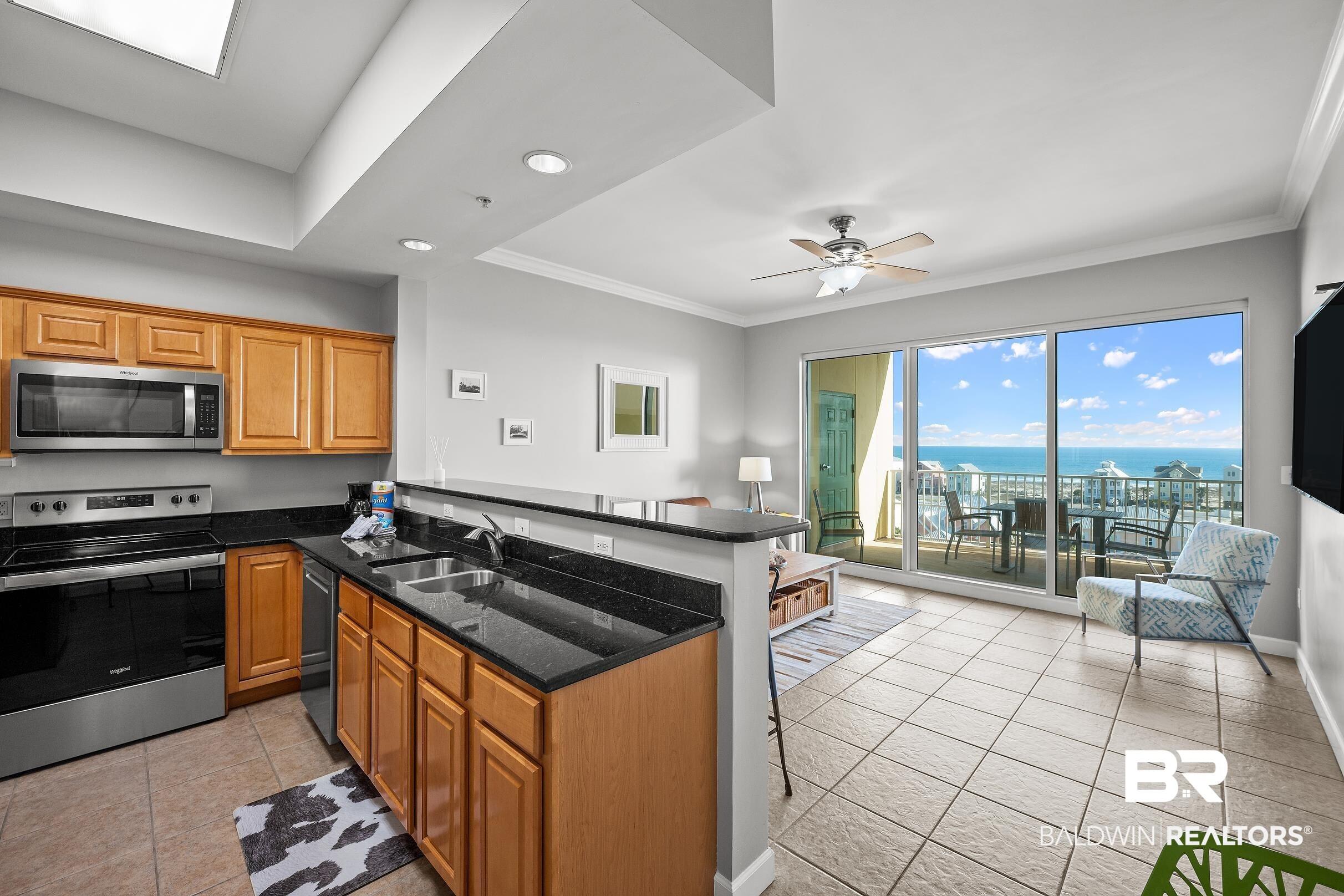 Image 3: Kitchen featuring stainless steel appliances, dark stone counters, a ceiling fan, open floor plan, and wood finish cabinetry