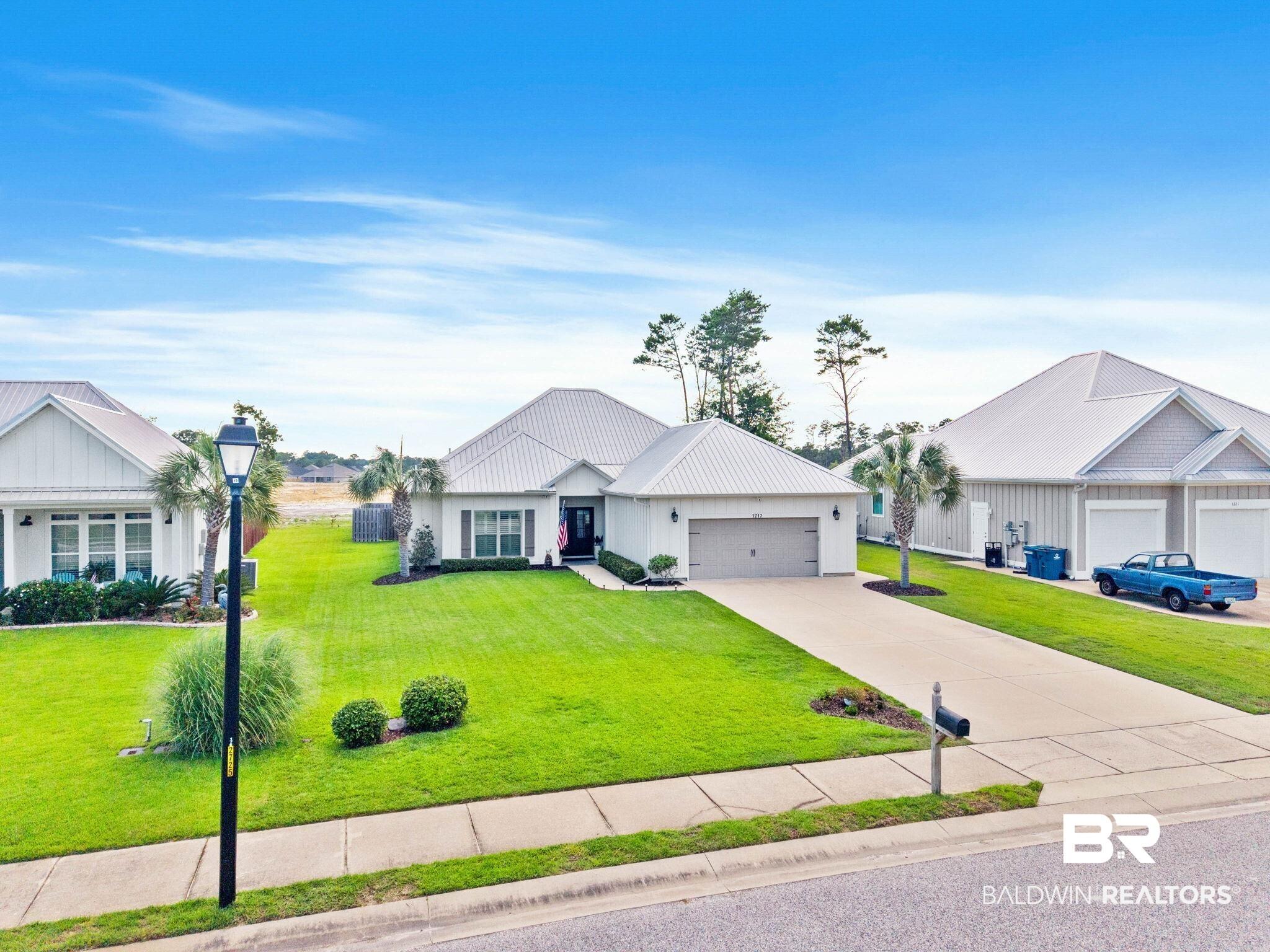 Image 2: Modern white exterior featuring a metal roof, attached garage, concrete driveway, and mature palm trees