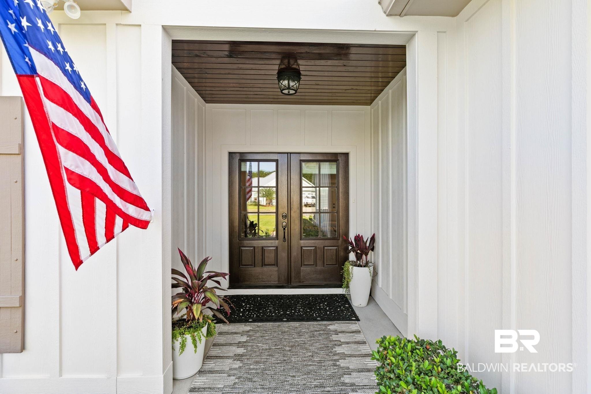 Image 4: Inviting entryway featuring a dark wood double door with glass panels, a rich wood-finish ceiling, and board and batten siding
