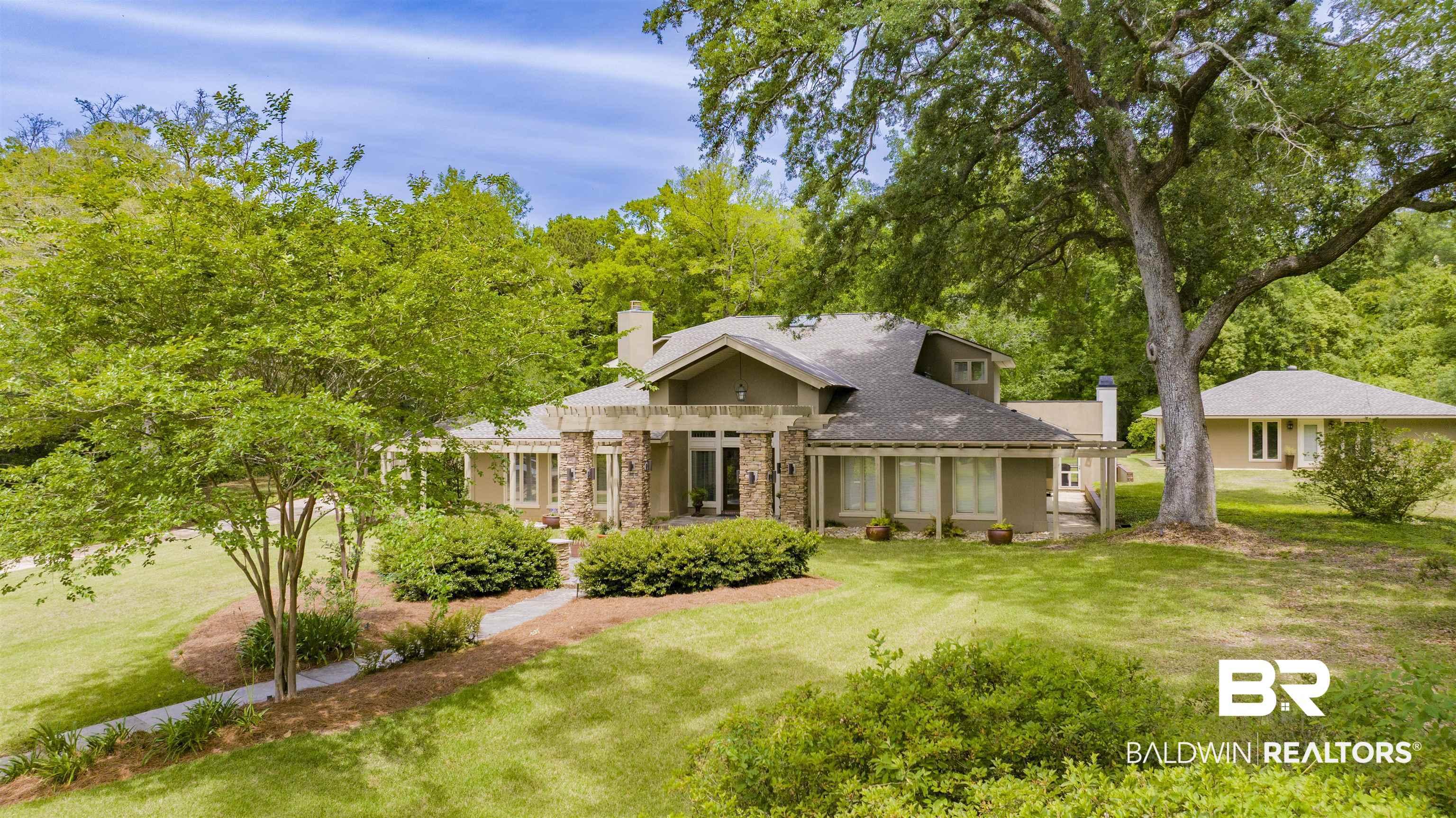 Image 2: Expansive green lawn surrounds a multi-level residence featuring a prominent stone facade, dark shingled roof, and an inviting stone pathway