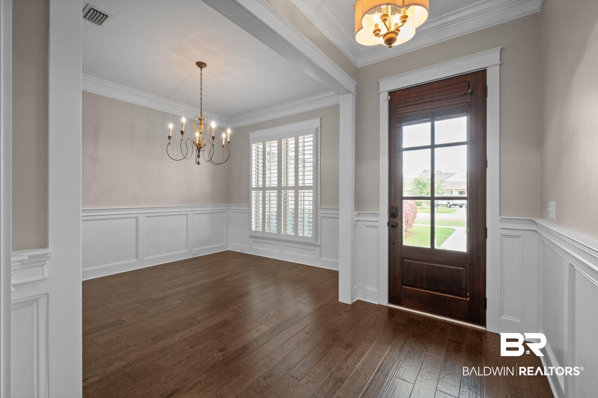 Image 3: Foyer entrance with suspended lighting, a wainscoted wall, ornamental molding, a decorative wall, and dark wood-style flooring
