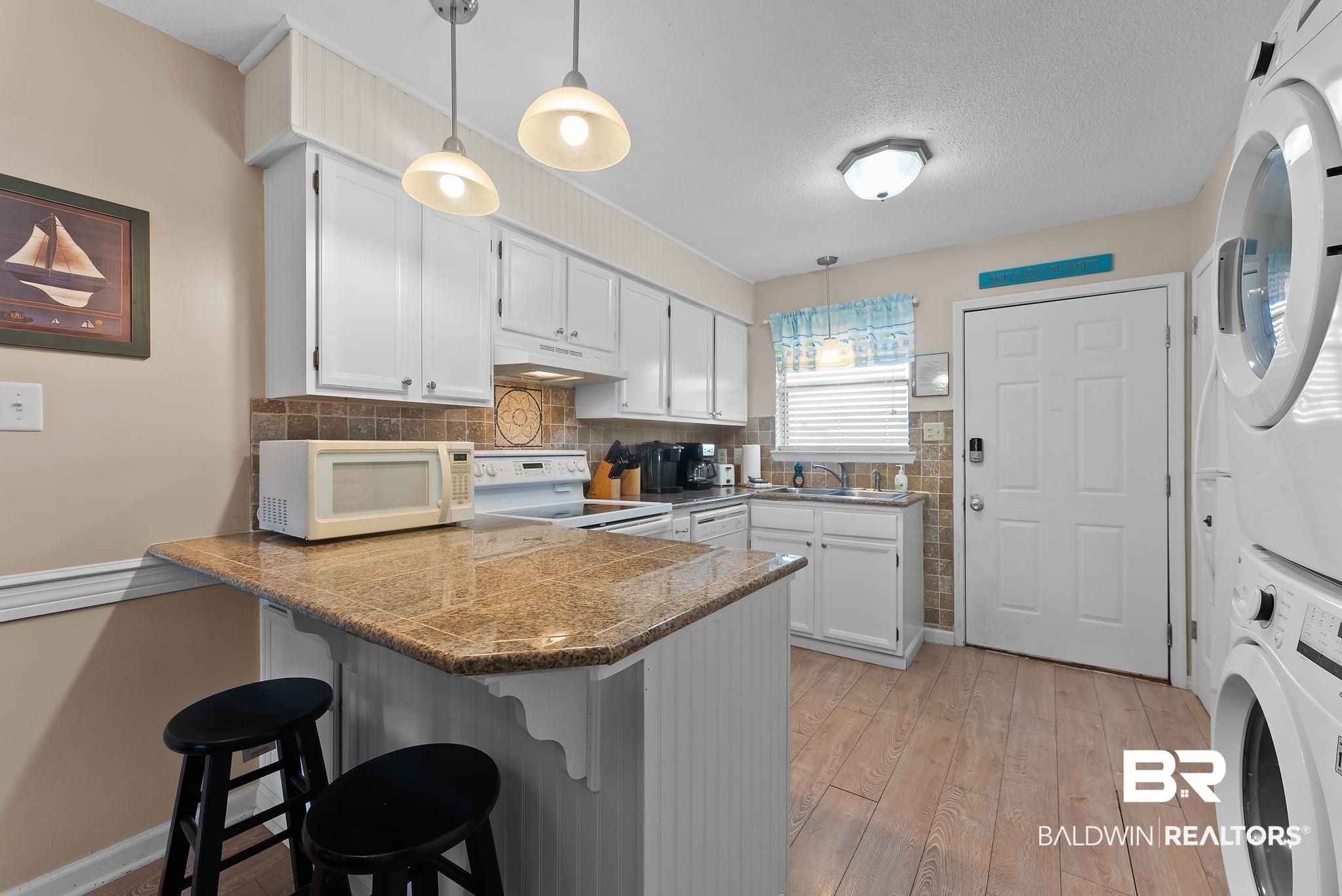 Image 3: Kitchen with a kitchen bar, a peninsula, hanging light fixtures, white cabinets, and a textured ceiling