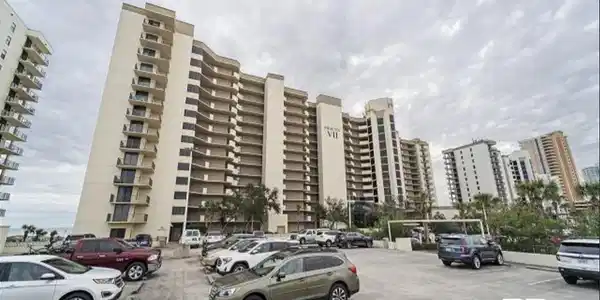 Image 3: Multi-story condominium building featuring numerous private balconies, a light-toned exterior, and an integrated parking area