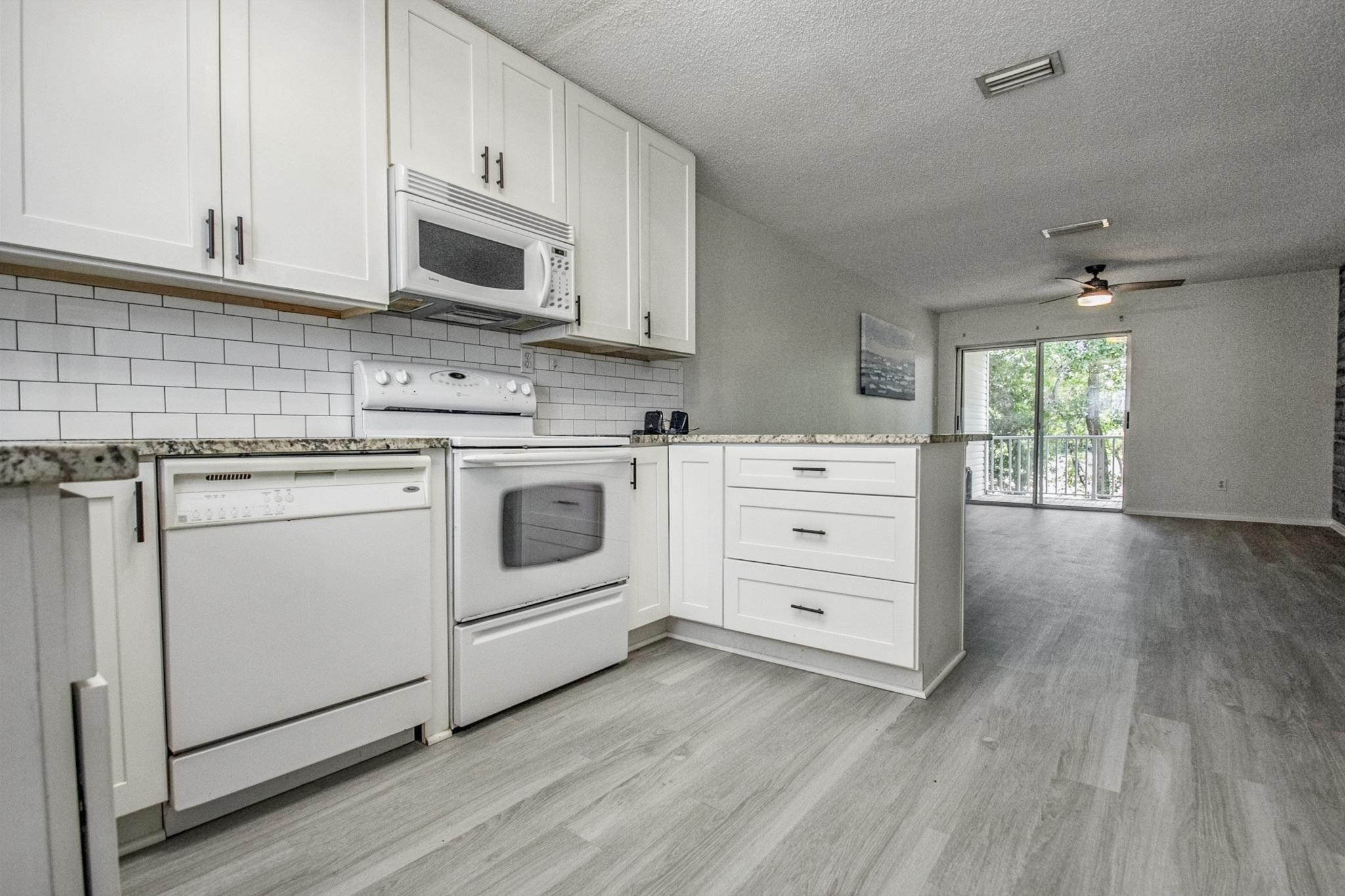 Image 3: Kitchen with white appliances, a textured ceiling, light stone countertops, white cabinets, and light wood-style floors