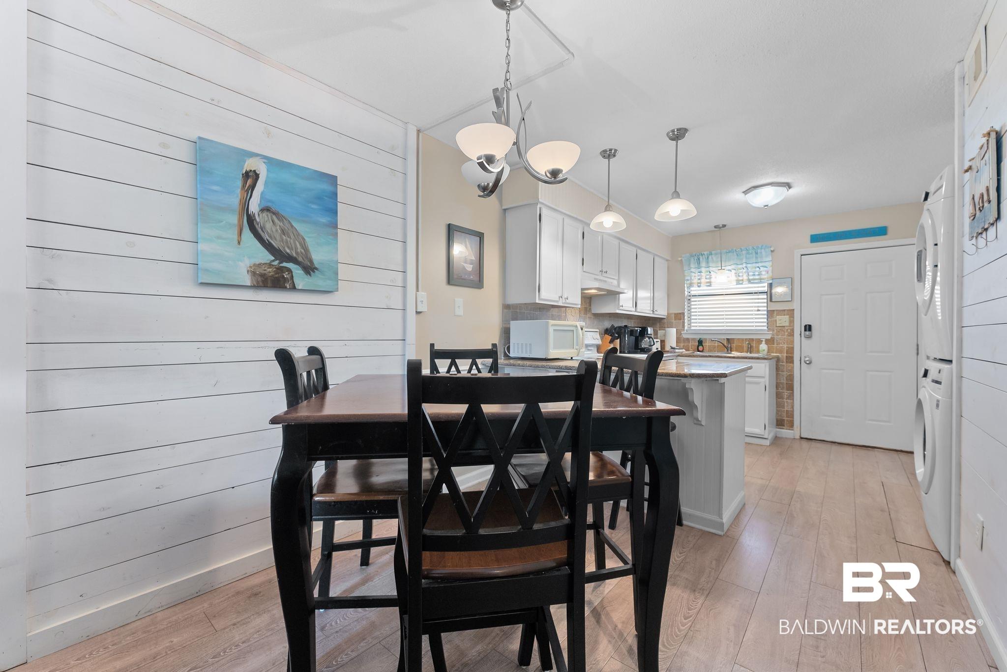 Image 4: Dining room with wood walls, stacked washer and clothes dryer, light wood finished floors, and suspended lighting