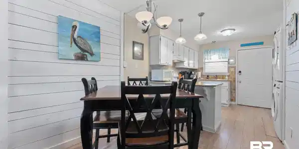 Image 4: Dining room with wood walls, stacked washer and clothes dryer, light wood finished floors, and suspended lighting