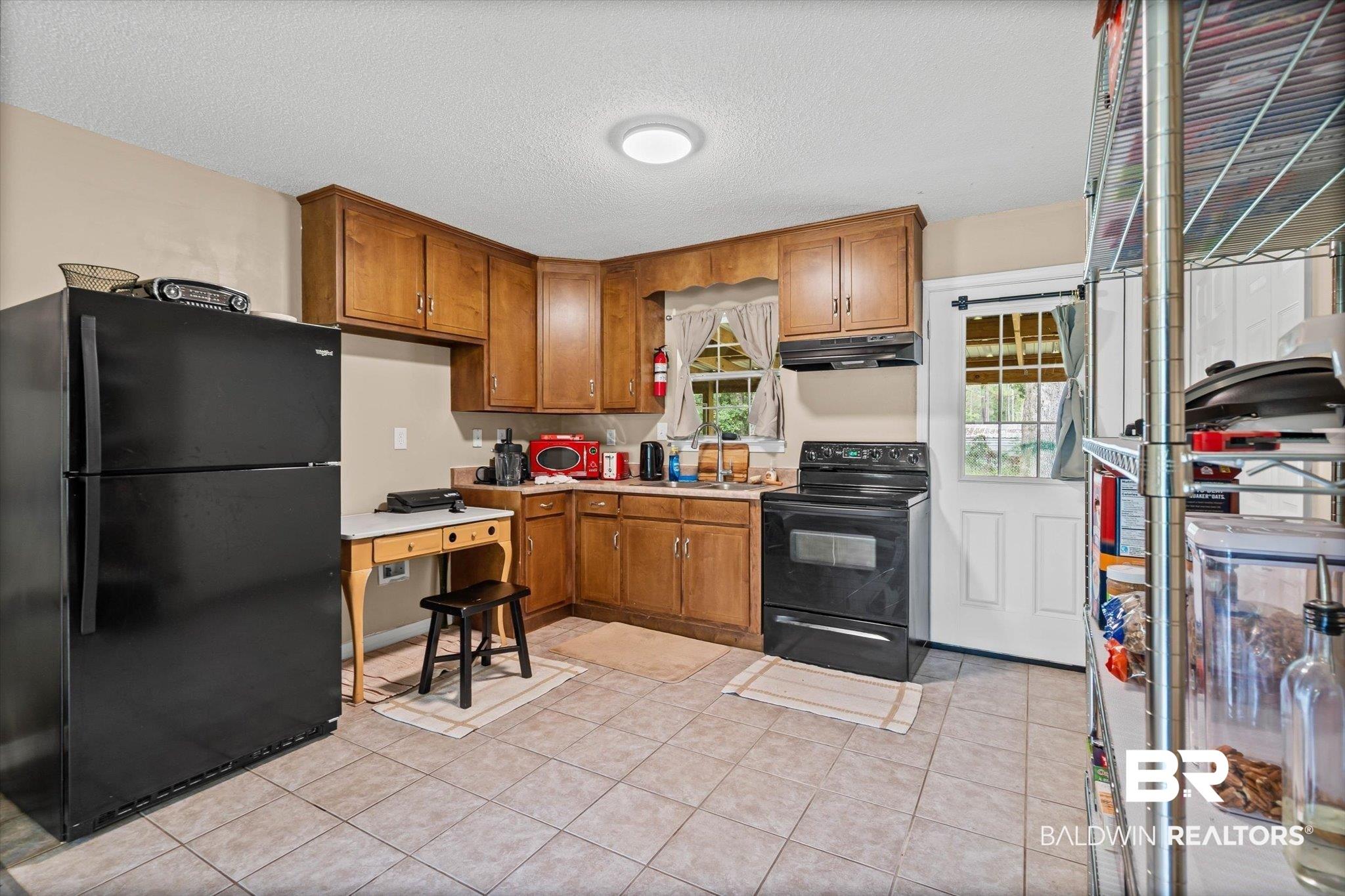 Image 4: Kitchen featuring black appliances, brown cabinetry, a textured ceiling, light countertops, and light tile patterned floors