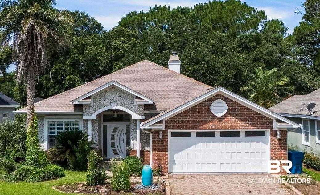 Image 4: Traditional-style residence featuring a brick and stone facade, a multi-pane front door, a two-car garage, an expansive paver driveway, and mature landscaping