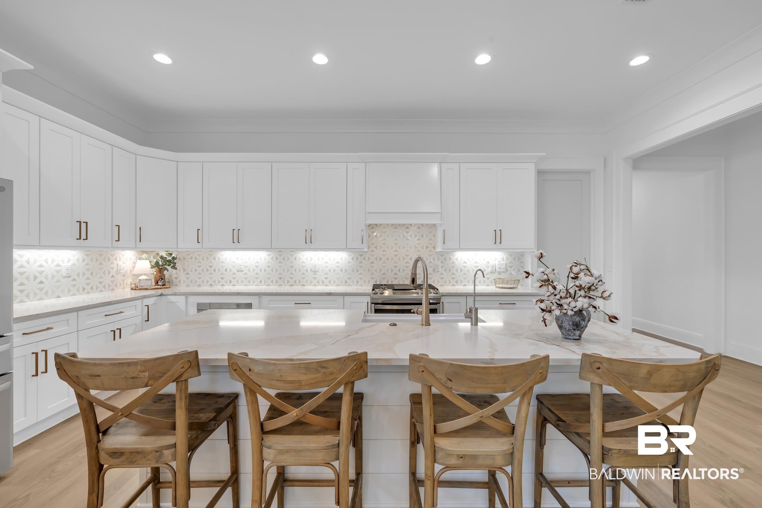 Image 2: Kitchen with light wood-style flooring, white cabinetry, light stone countertops, recessed lighting, and a kitchen bar