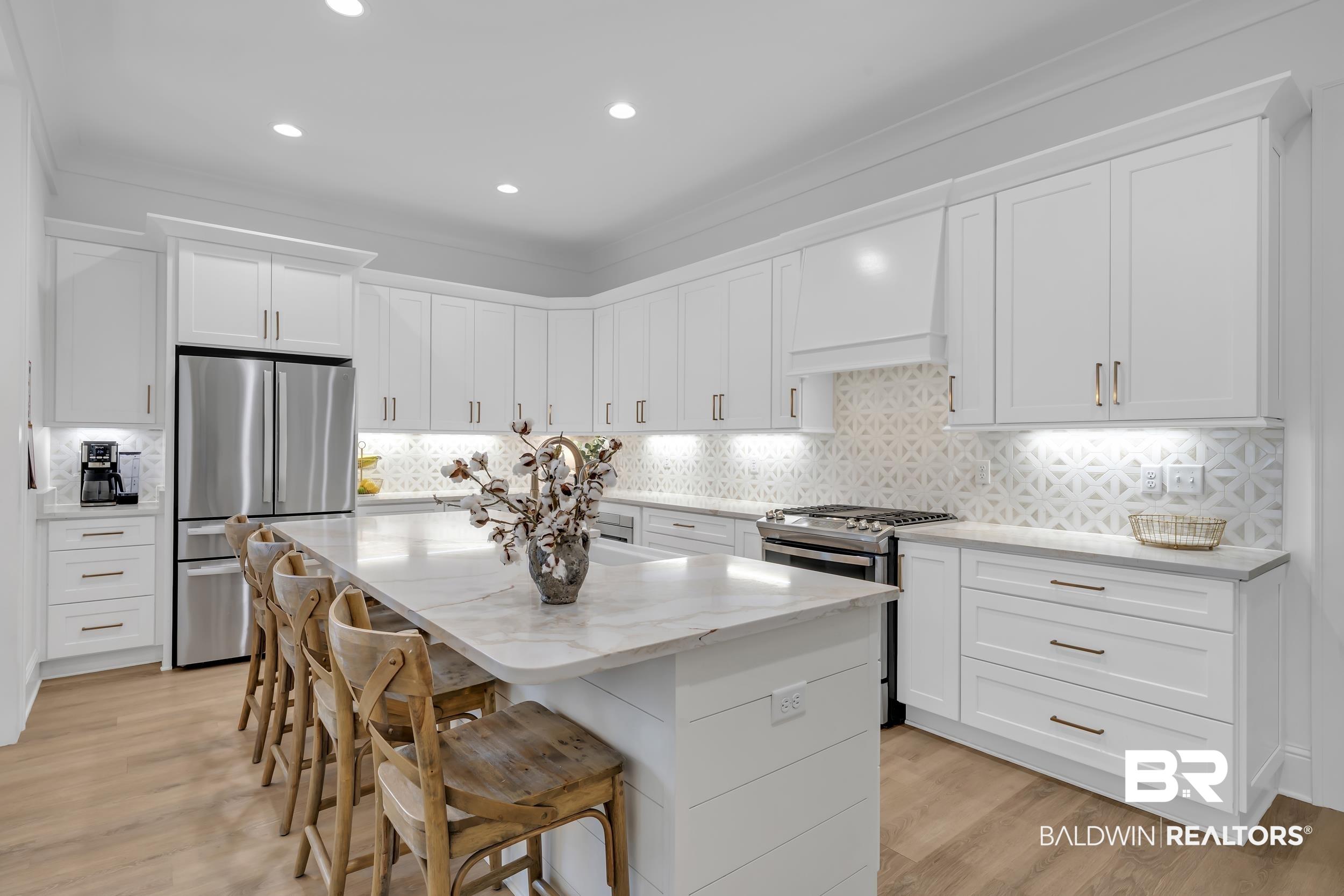 Image 3: Kitchen with white cabinets, a kitchen bar, stainless steel appliances, light wood-style floors, and a kitchen island