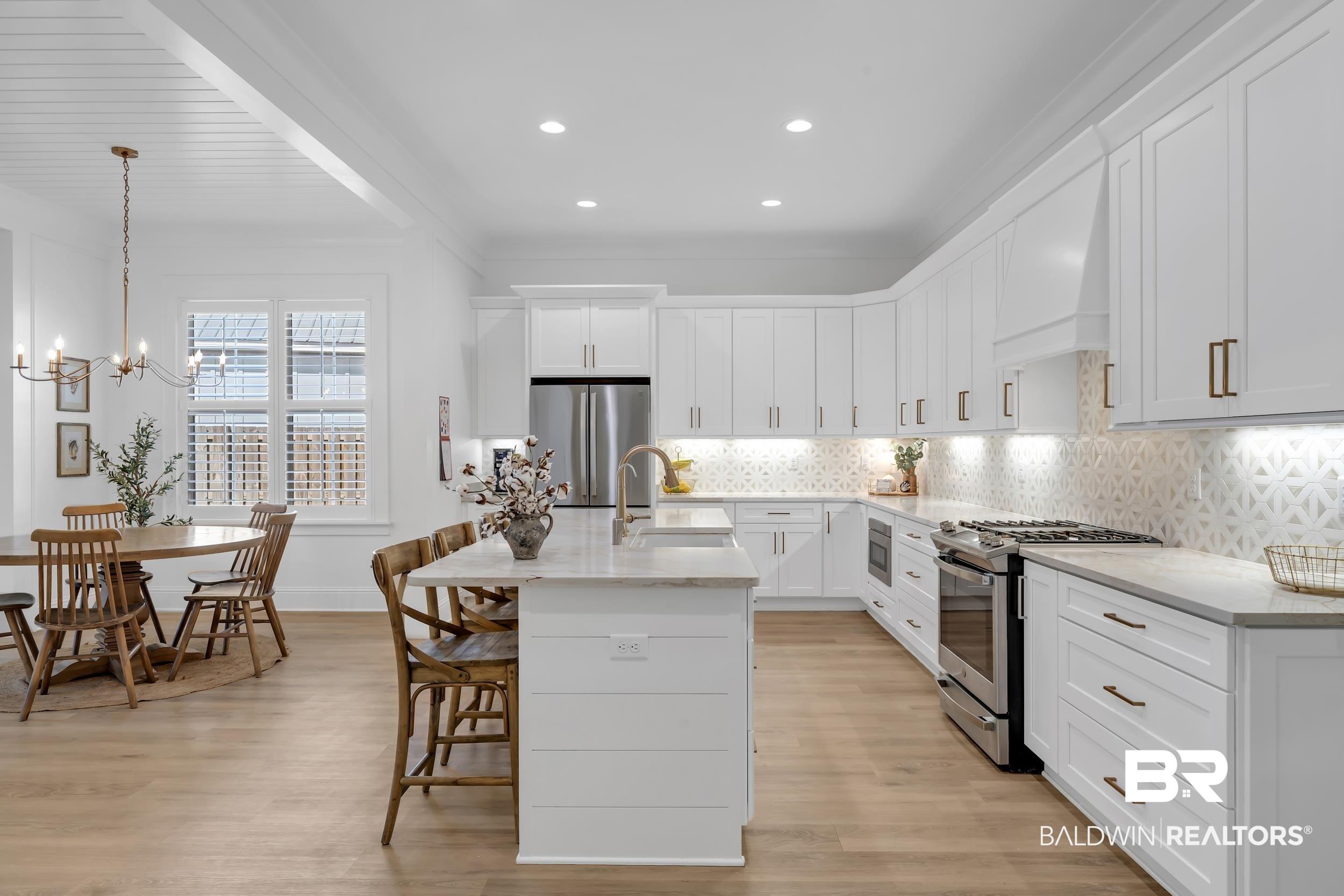 Image 4: Kitchen with stainless steel appliances, decorative backsplash, white cabinets, light stone counters, and a center island with sink