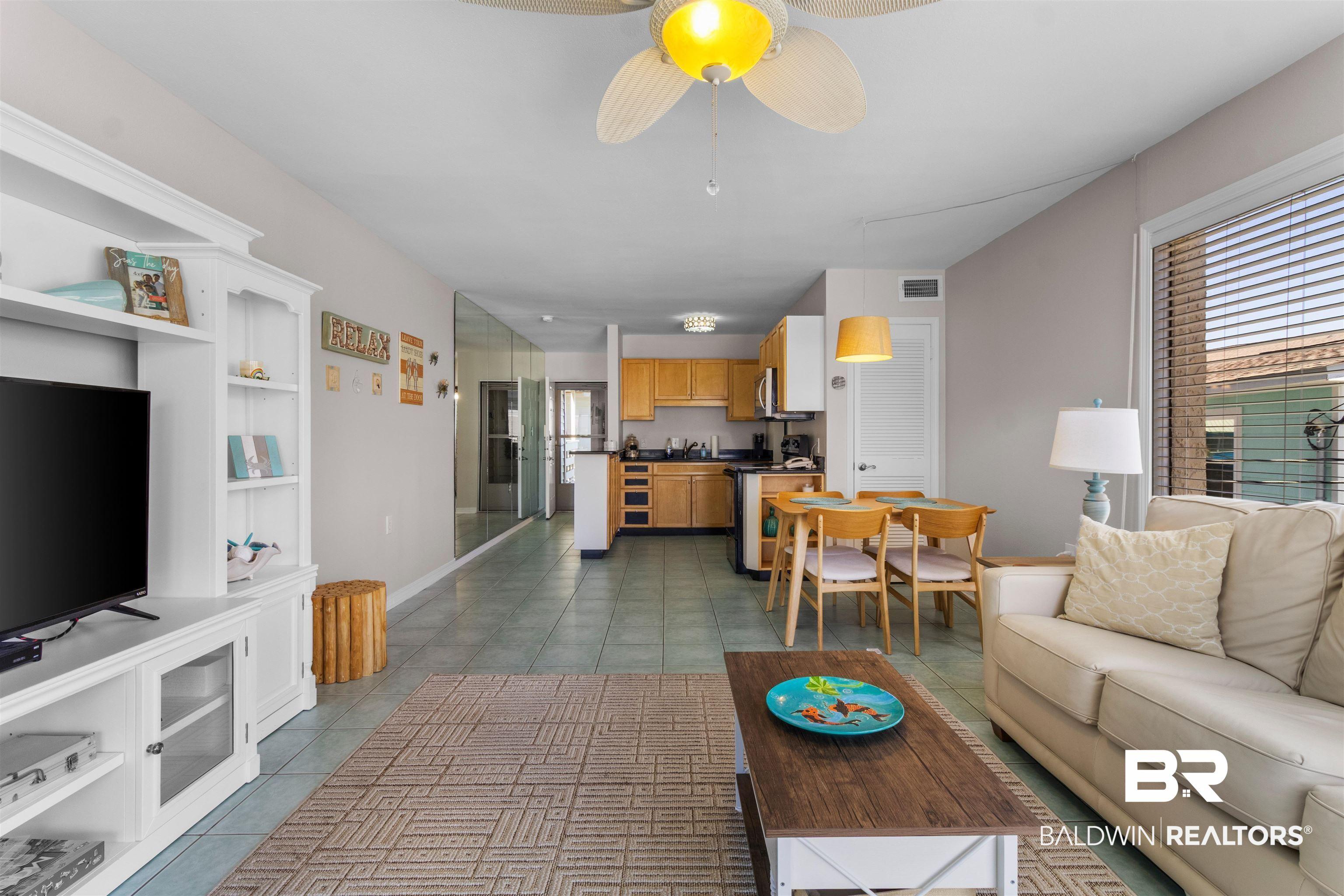 Image 3: Open-concept living area with tile flooring throughout, featuring a built-in media console, ceiling fan with integrated lighting, and a dining area with pendant lighting