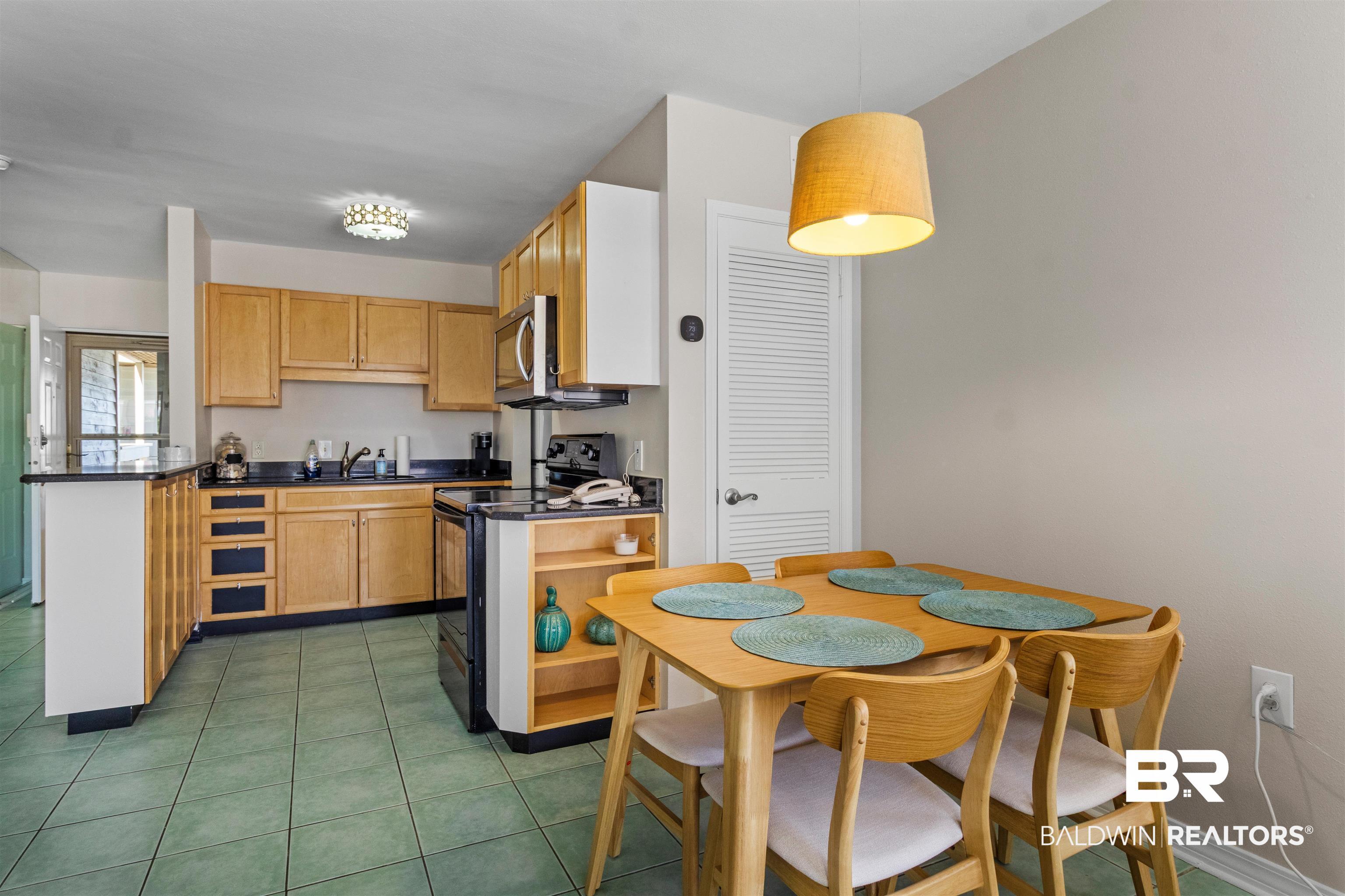 Image 4: Open-concept kitchen and dining area featuring wood-finish cabinetry, dark countertops, and integrated stainless steel appliances