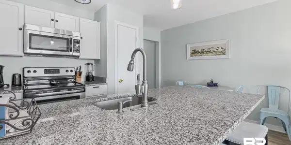 Image 2: Kitchen featuring stainless steel appliances, light stone countertops, white cabinetry, hanging light fixtures, and a breakfast bar