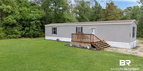 Image 2: Single-story residence featuring gray horizontal siding and a light-colored foundation skirting