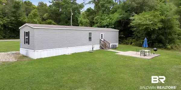 Image 3: Single-story residence featuring gray horizontal siding and a white foundation skirt