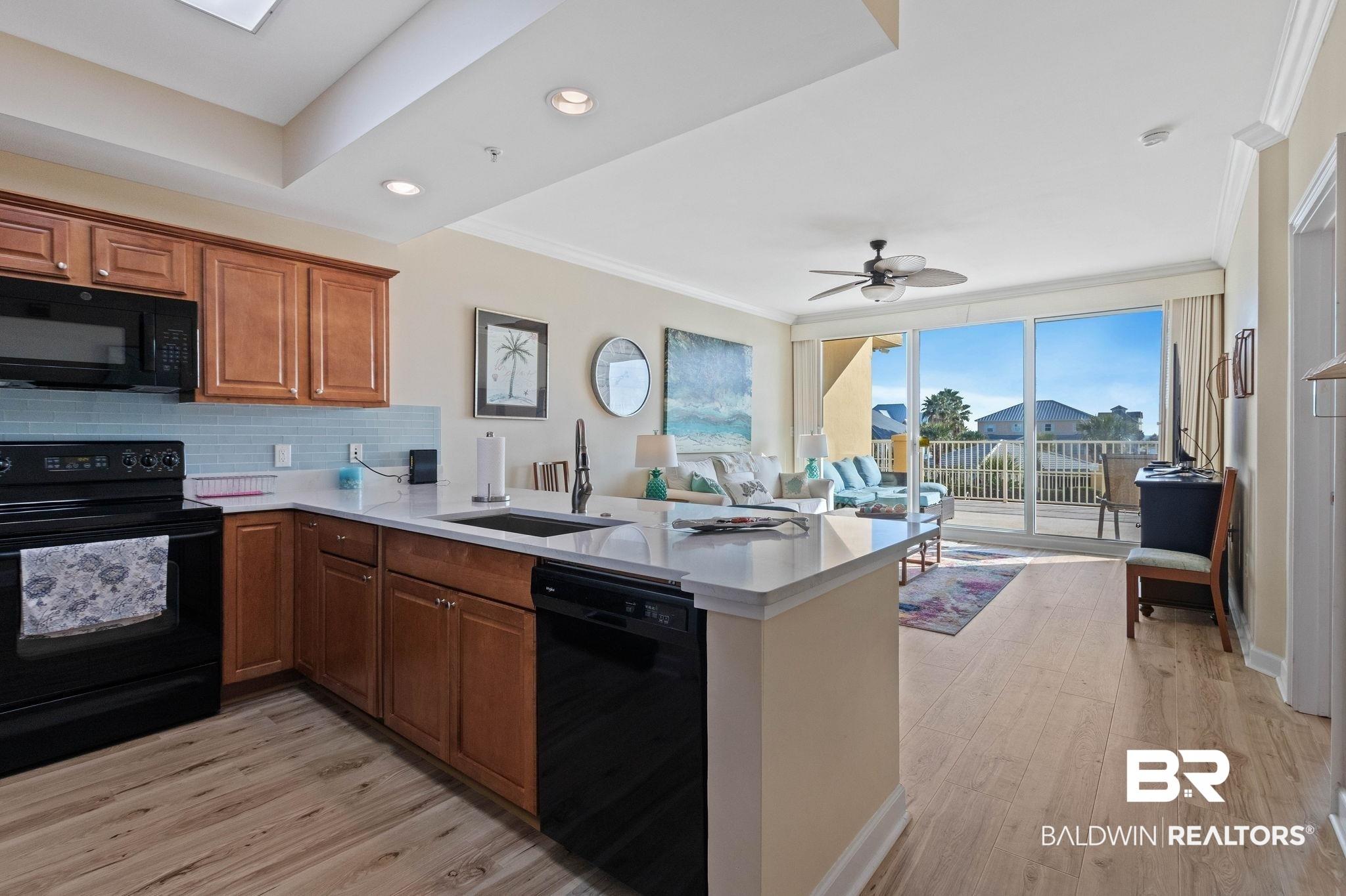 Image 4: Kitchen featuring black appliances, brown cabinets, tasteful backsplash, light wood-style flooring, and crown molding