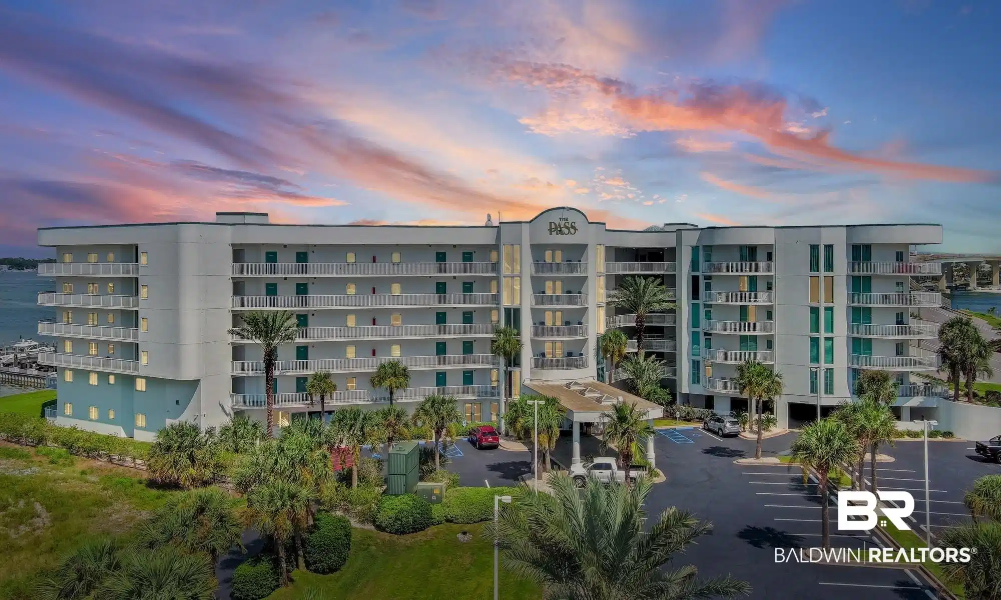 Image 1: Multi-story condominium building featuring private balconies, a covered entrance, and expansive parking areas