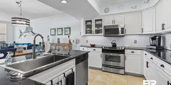 Image 2: Open-concept kitchen featuring white cabinetry, dark stone countertops, stainless steel appliances, a subway tile backsplash, and tile flooring