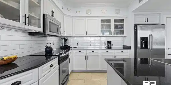 Image 4: Kitchen featuring white cabinetry, black stone countertops, stainless steel appliances, a subway tile backsplash, and light-toned tile flooring