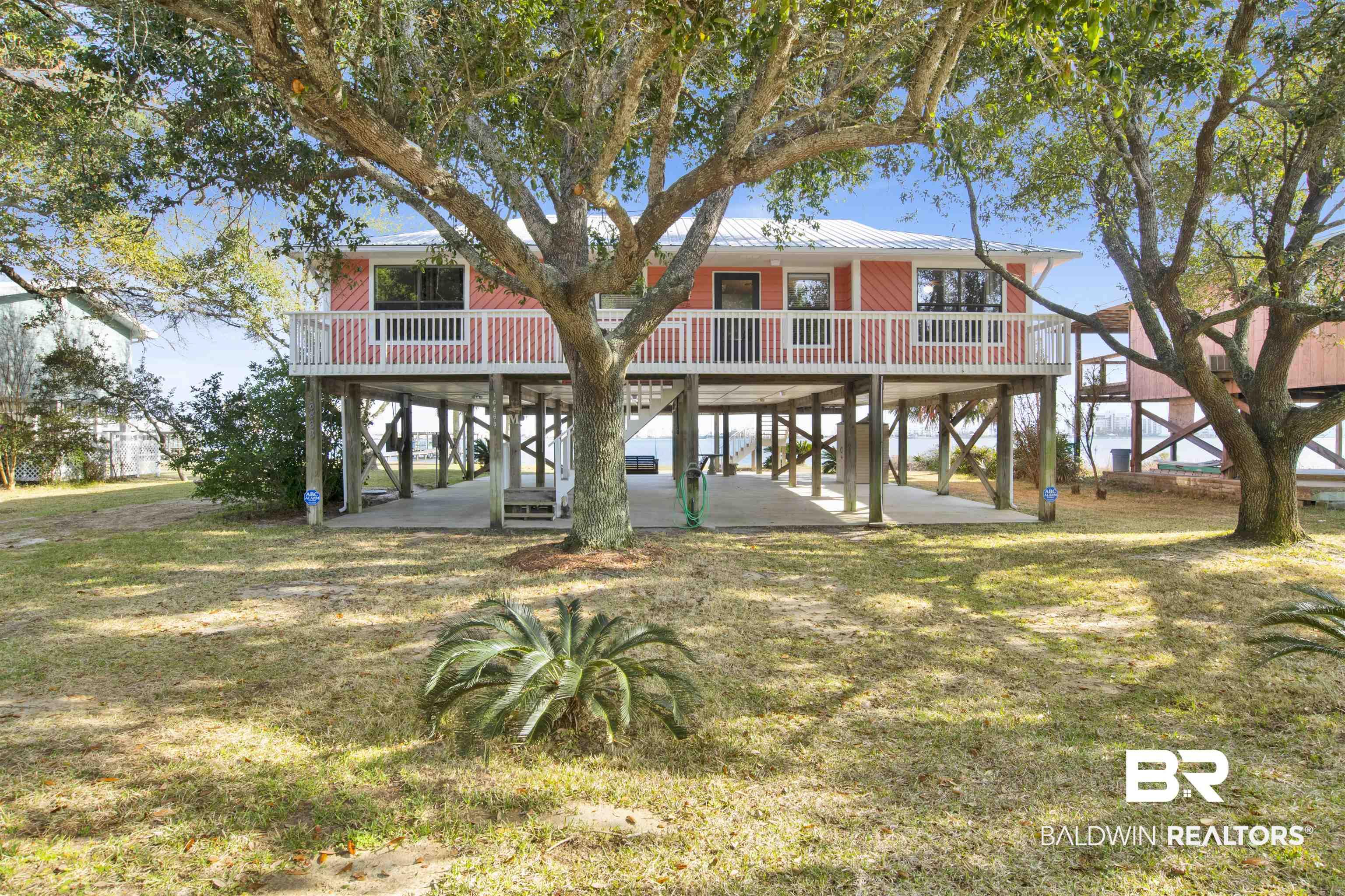 Image 2: View of front facade featuring a wooden deck, a patio area, a front yard, a carport, and a metal roof