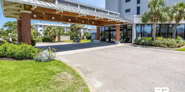 Image 4: Building entrance with a covered drive-through, glass double doors, brick-clad columns, and a white multi-story exterior