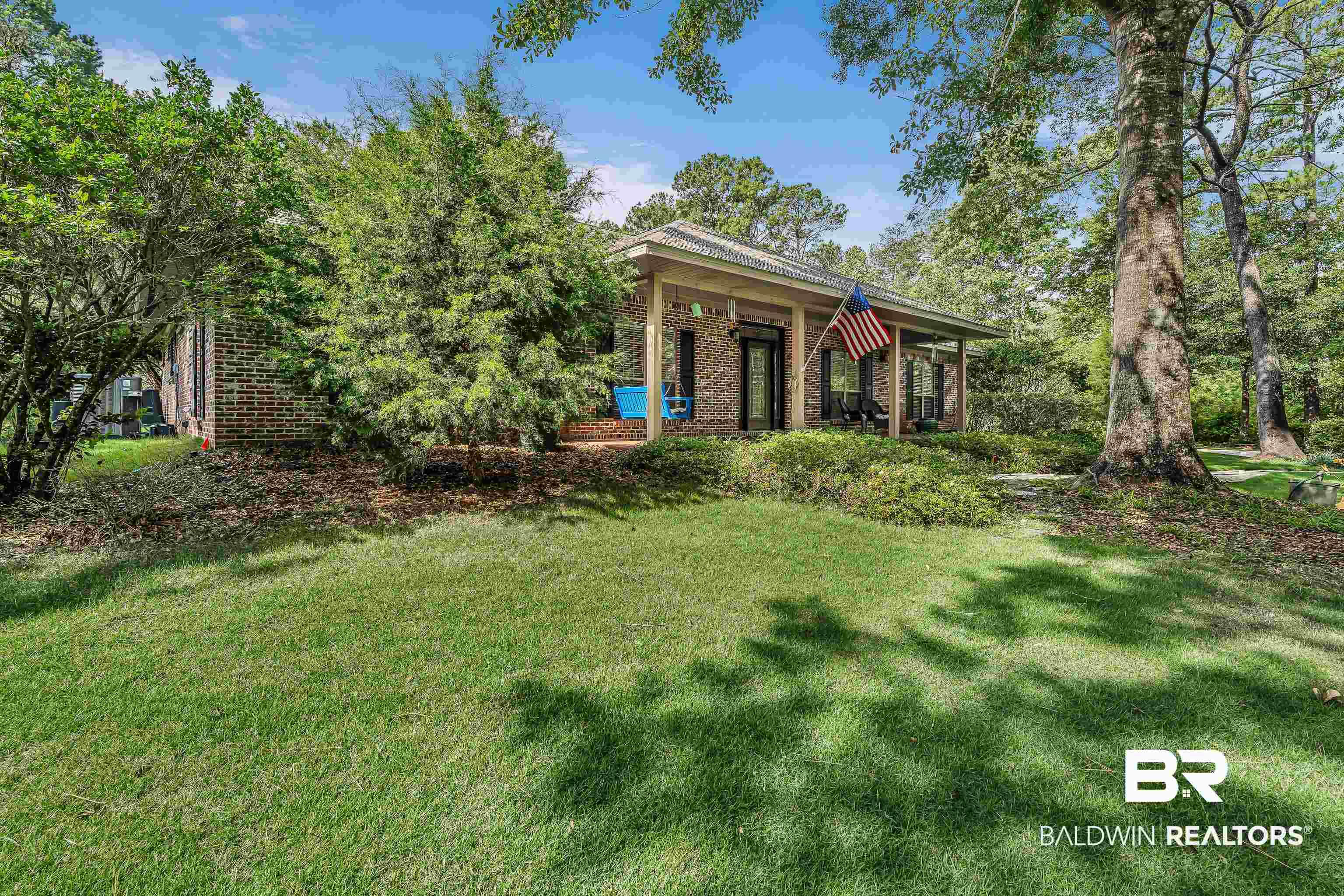Image 2: Brick exterior residence featuring a covered front porch, mature trees, landscaped shrubbery, and a manicured lawn