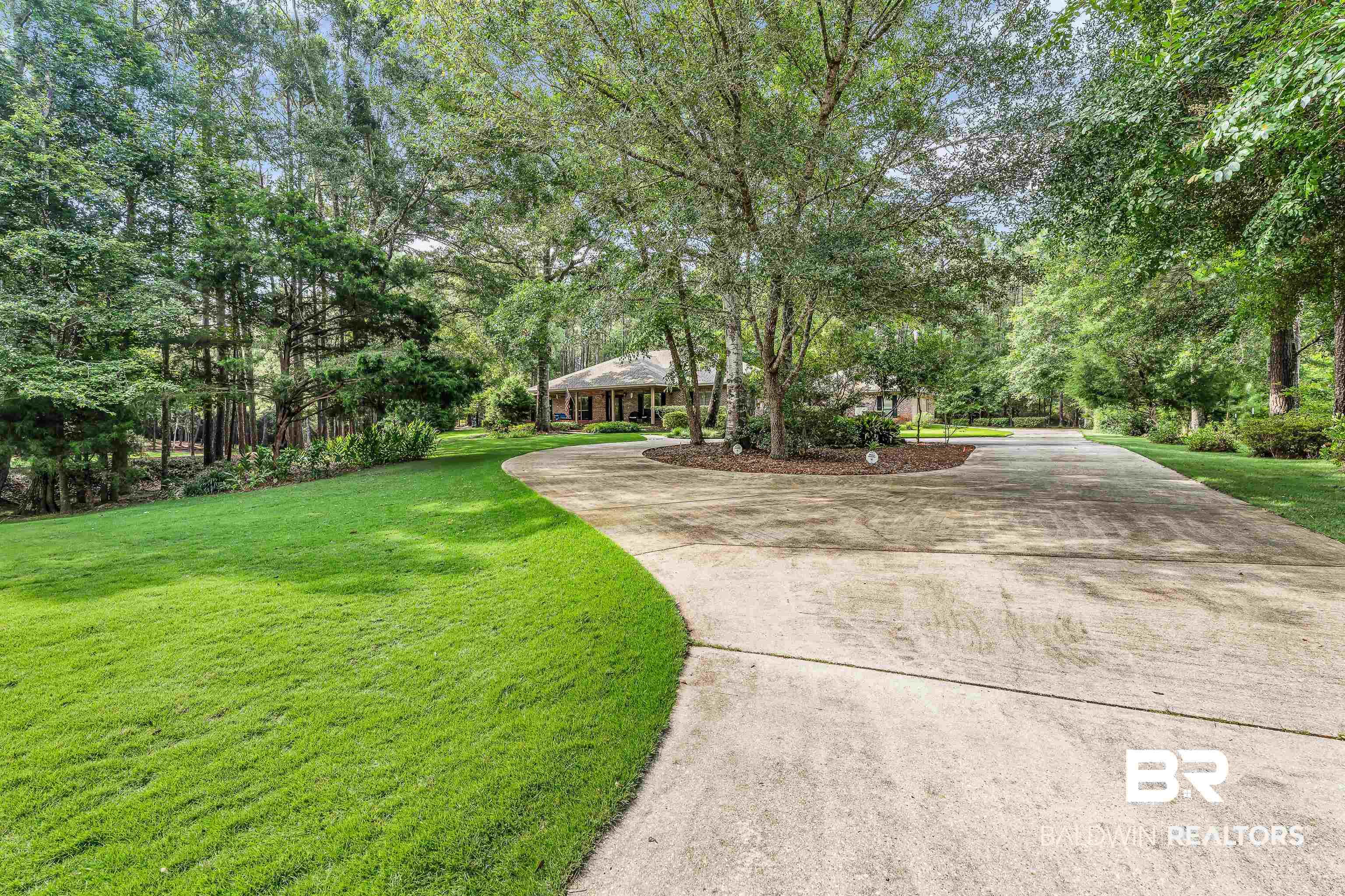 Image 3: Expansive concrete driveway with a central circular island, framed by mature trees and lush green lawns