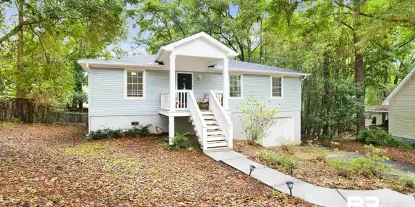 Image 2: Light blue siding exterior featuring a white covered porch with railing and steps, white window trim, and a concrete pathway with small light fixtures